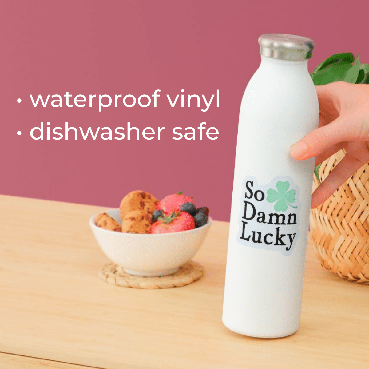 White water bottle with 'So Damn Lucky' text on a wooden table with a bowl of fruit and cookies.