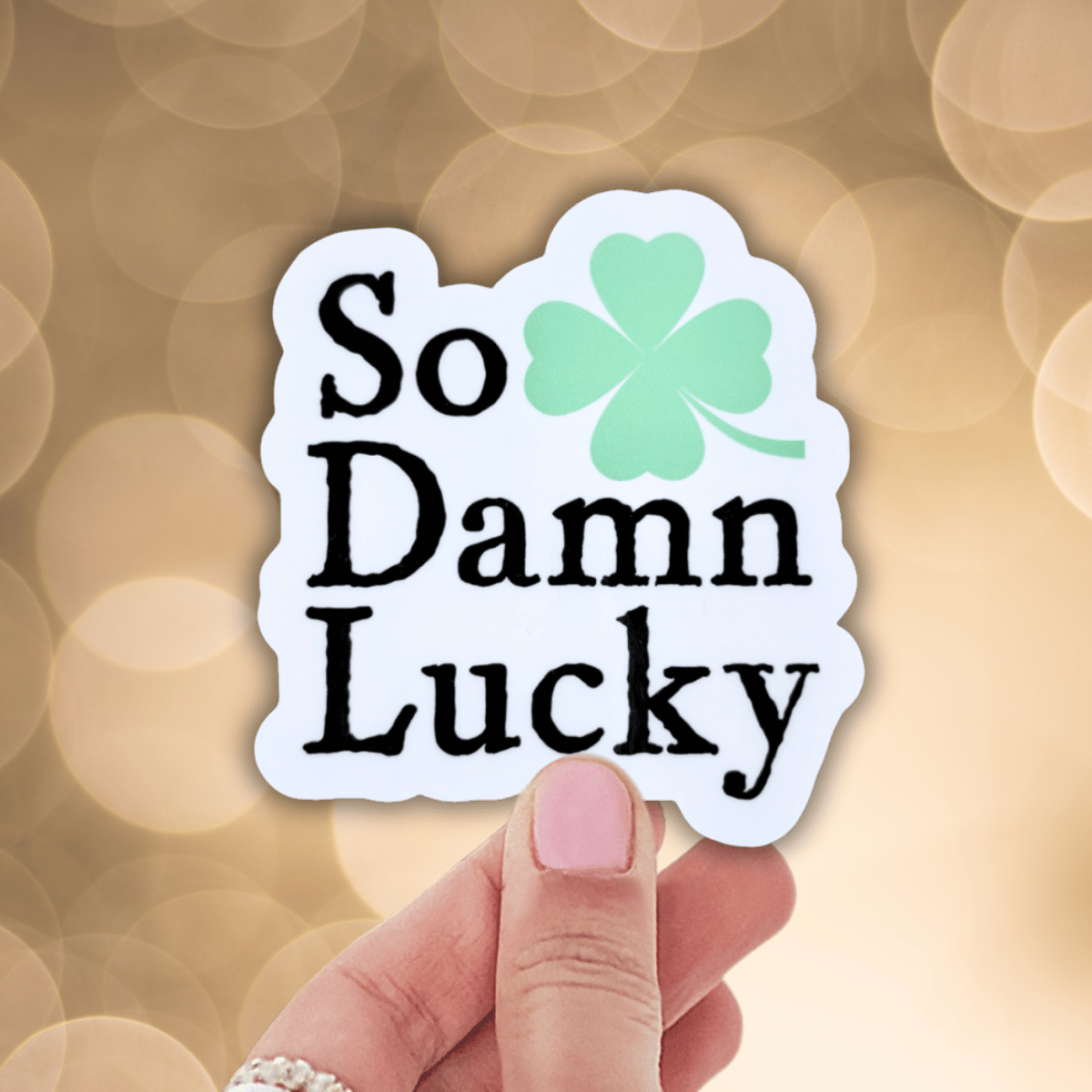 Sticker with 'So Damn Lucky' text and a four-leaf clover on a blurred background