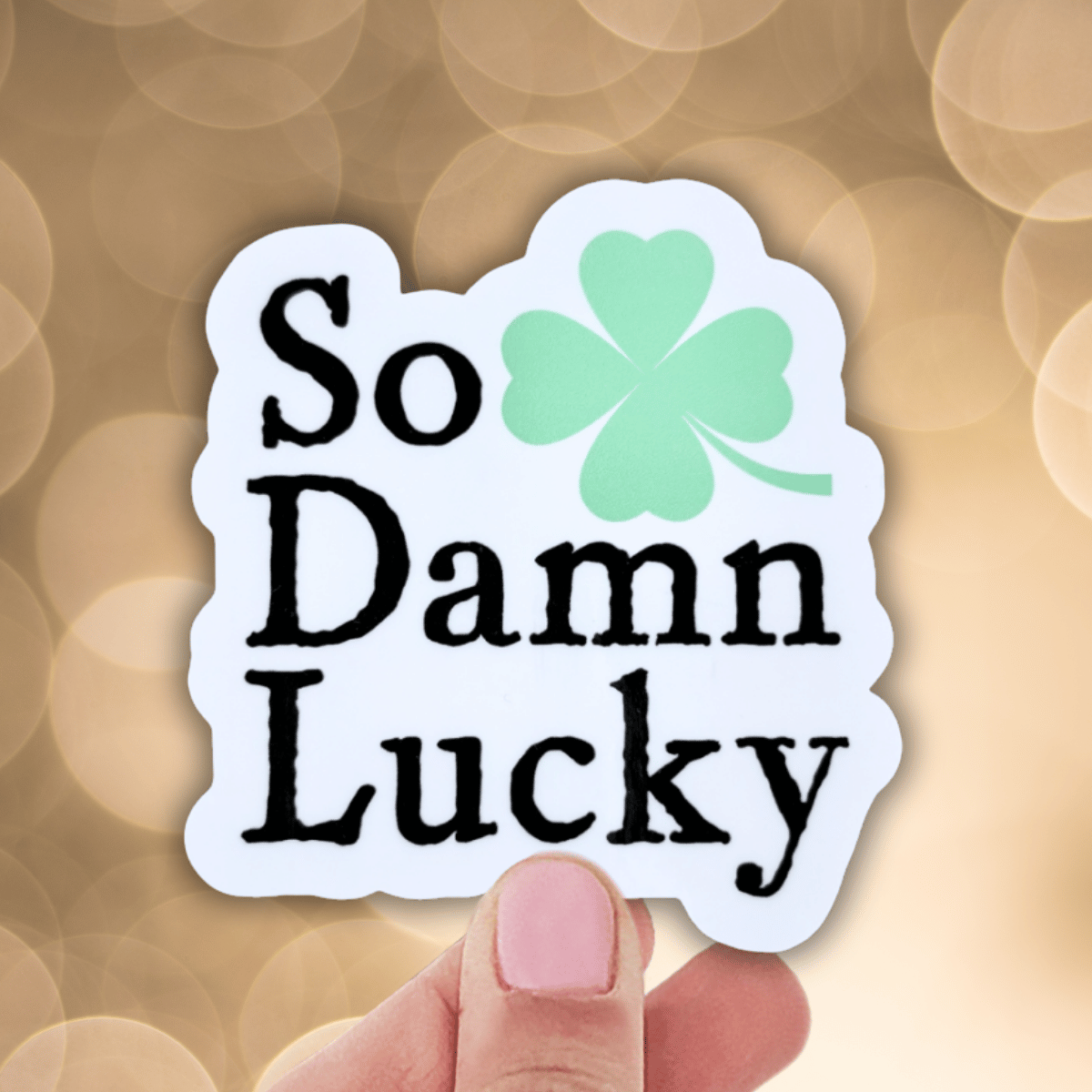 Sticker with 'So Damn Lucky' text and a four-leaf clover on a blurred background