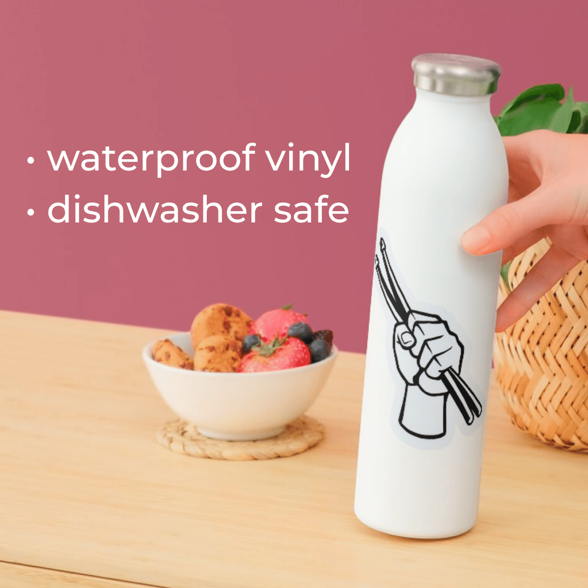 White water bottle with a design on a wooden table with a bowl of fruit and a pink background.