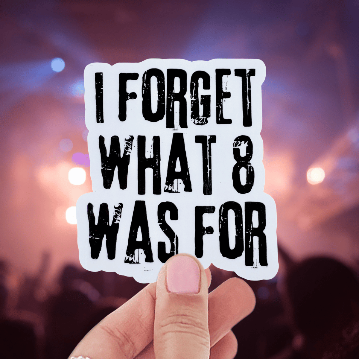 Hand holding a sticker with text 'I FORGET WHAT 8 WAS FOR' against a blurred concert background.
