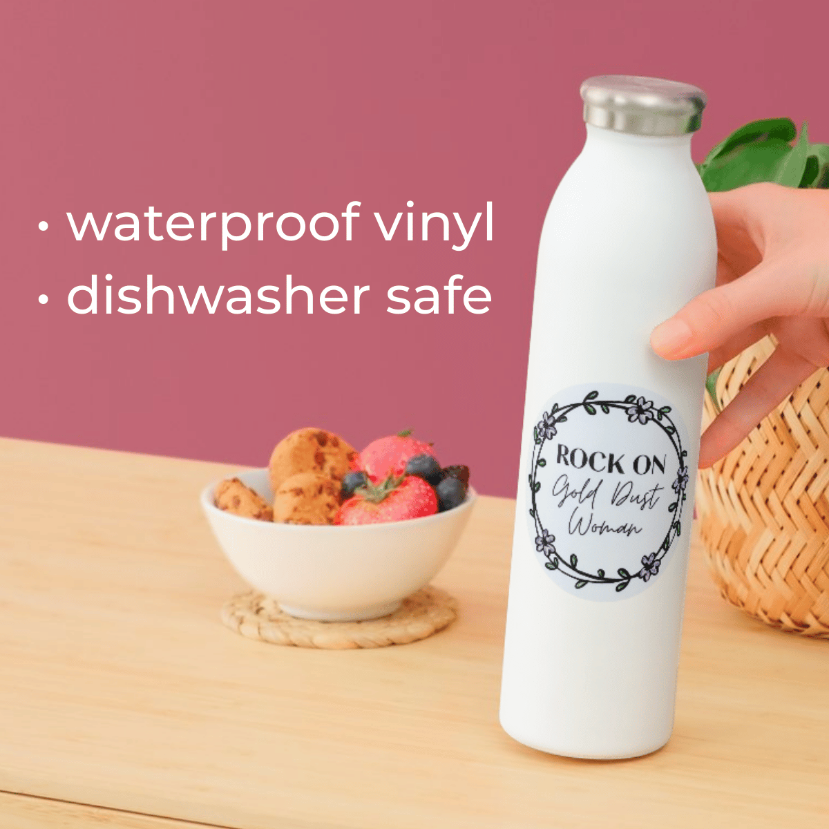 White water bottle with black text on a wooden table with a bowl of fruit and a pink background.