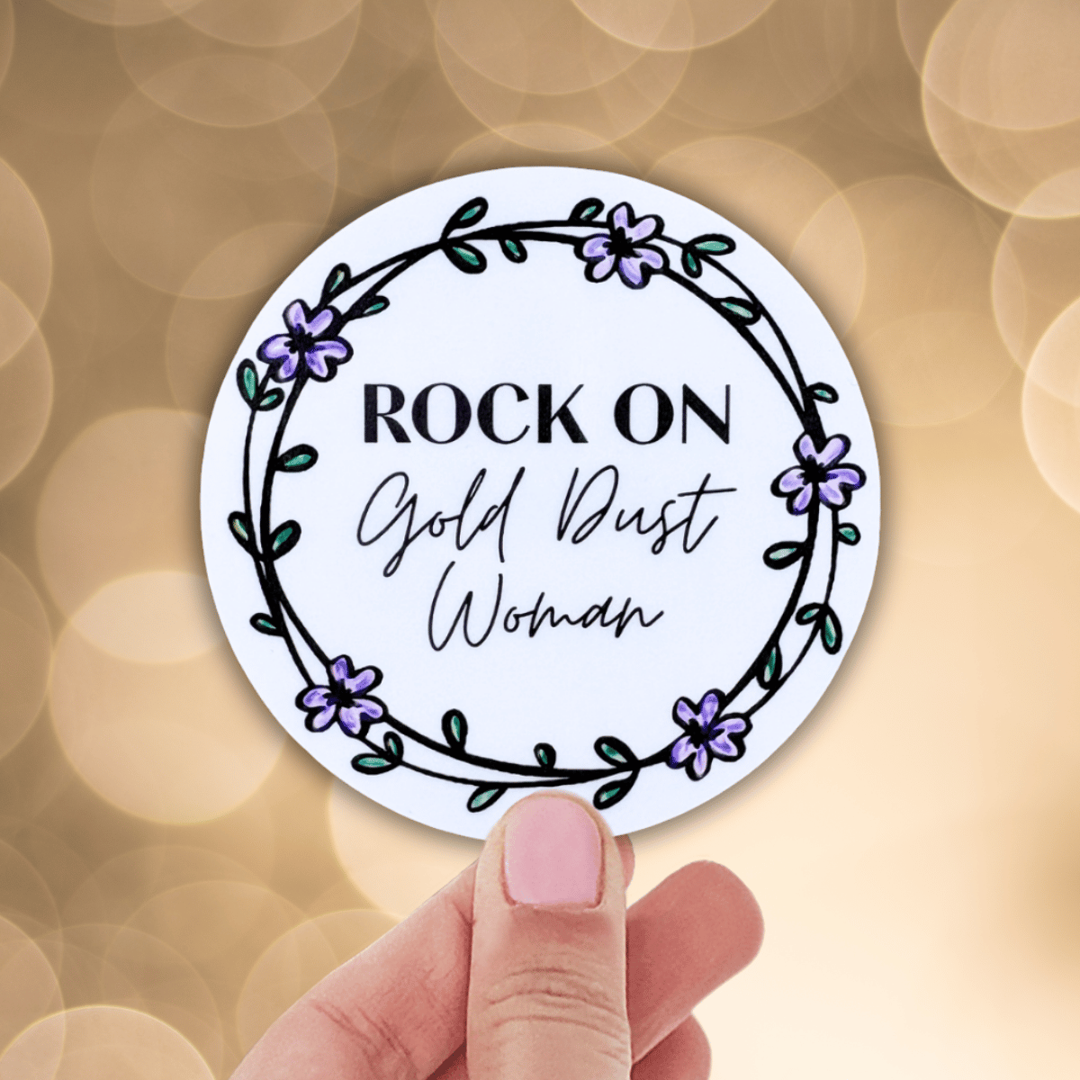 Circular sticker with 'Rock On Gold Dust Woman' text held by a hand against a blurred background