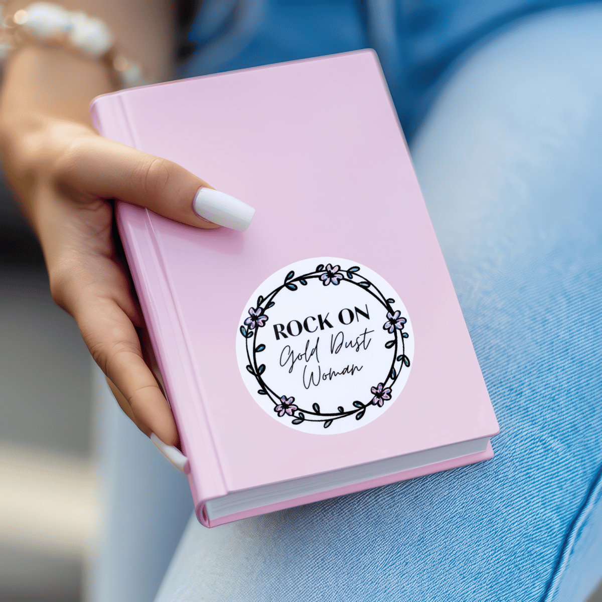 Pink notebook with a sticker on it held by a hand, against a blurred background