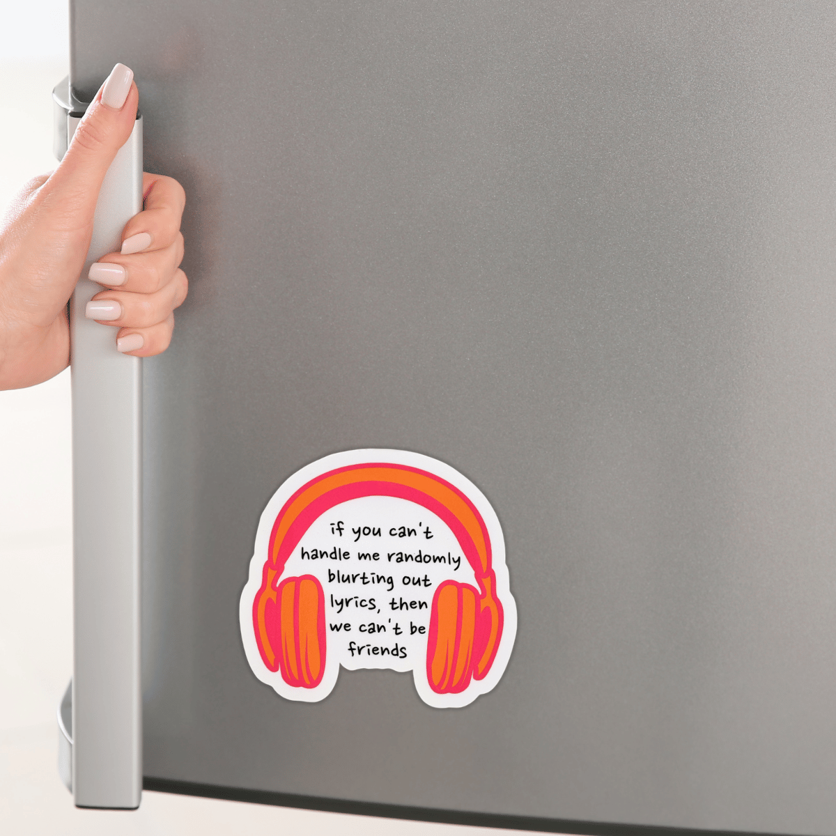 Fridge with a sticker of headphones and text, held by a hand.