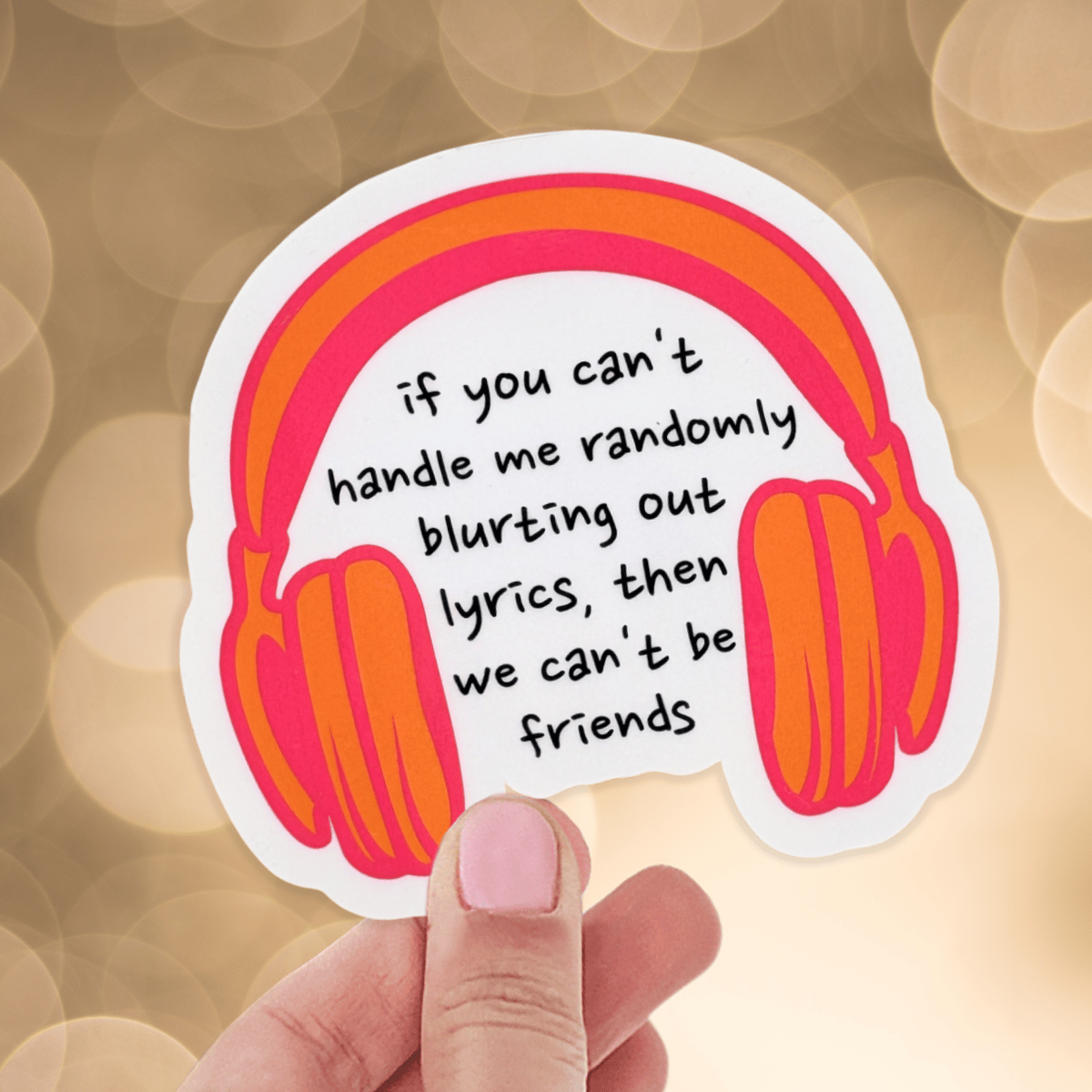 Sticker with headphones and text held by a hand against a blurred background