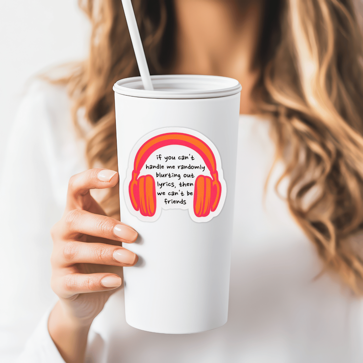 Person holding a white tumbler with a colorful sticker featuring headphones and text.