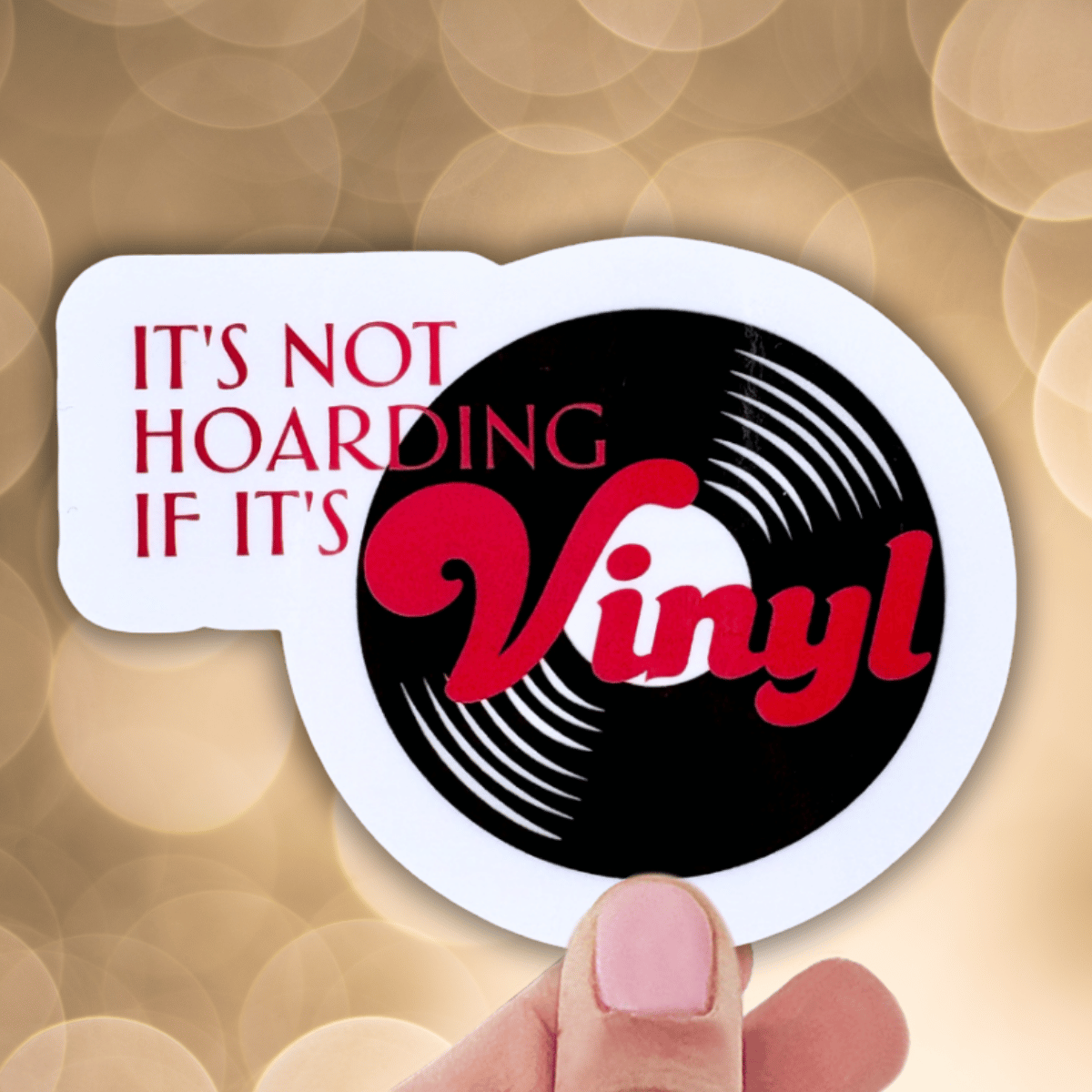Sticker with vinyl record design and text 'It's not hoarding if it's vinyl' held by a hand against a blurred background.
