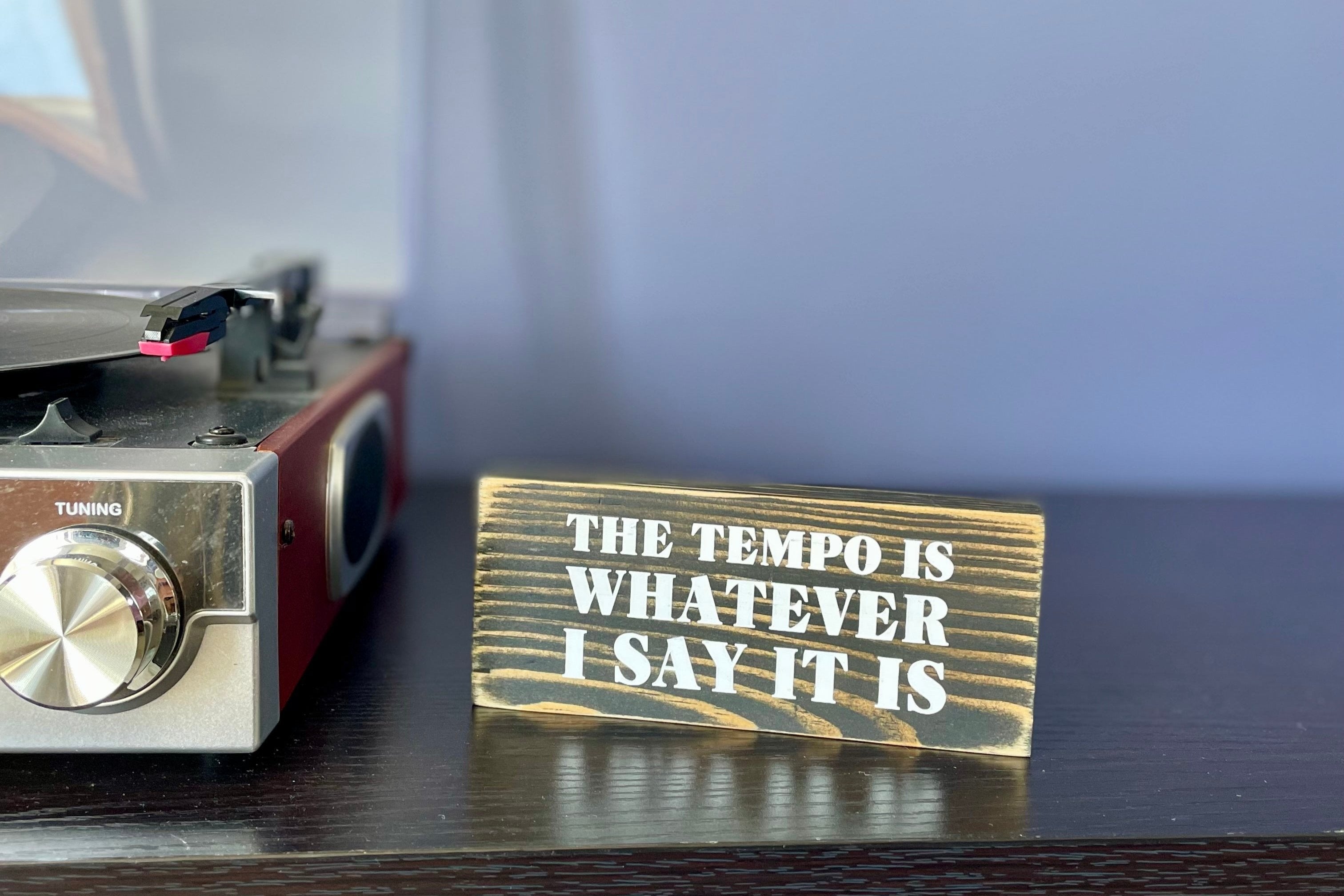 A small, black, wood sign sits on a table next to a record player