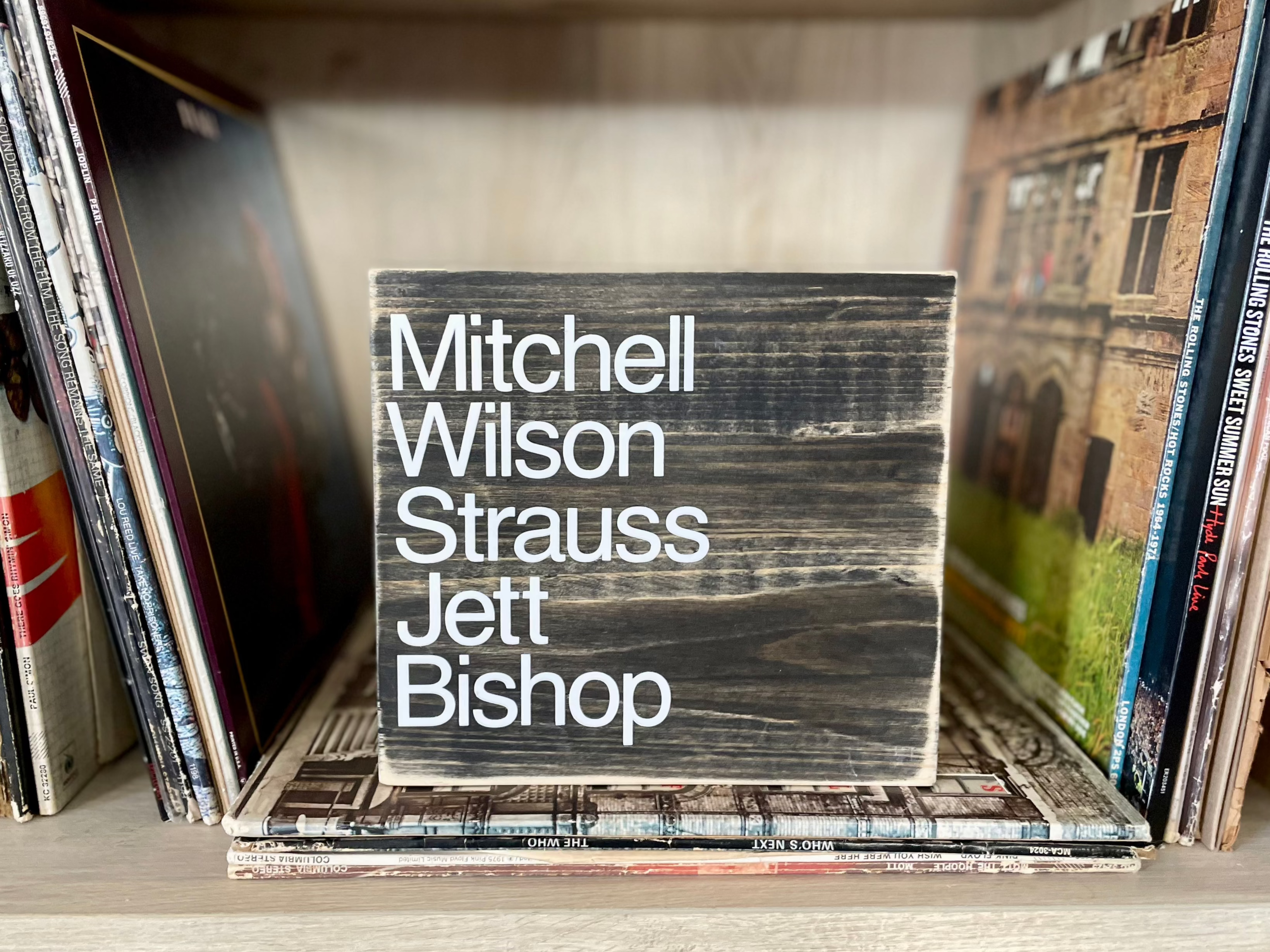 A square, black, wood sign sits on a shelf of vinyl records