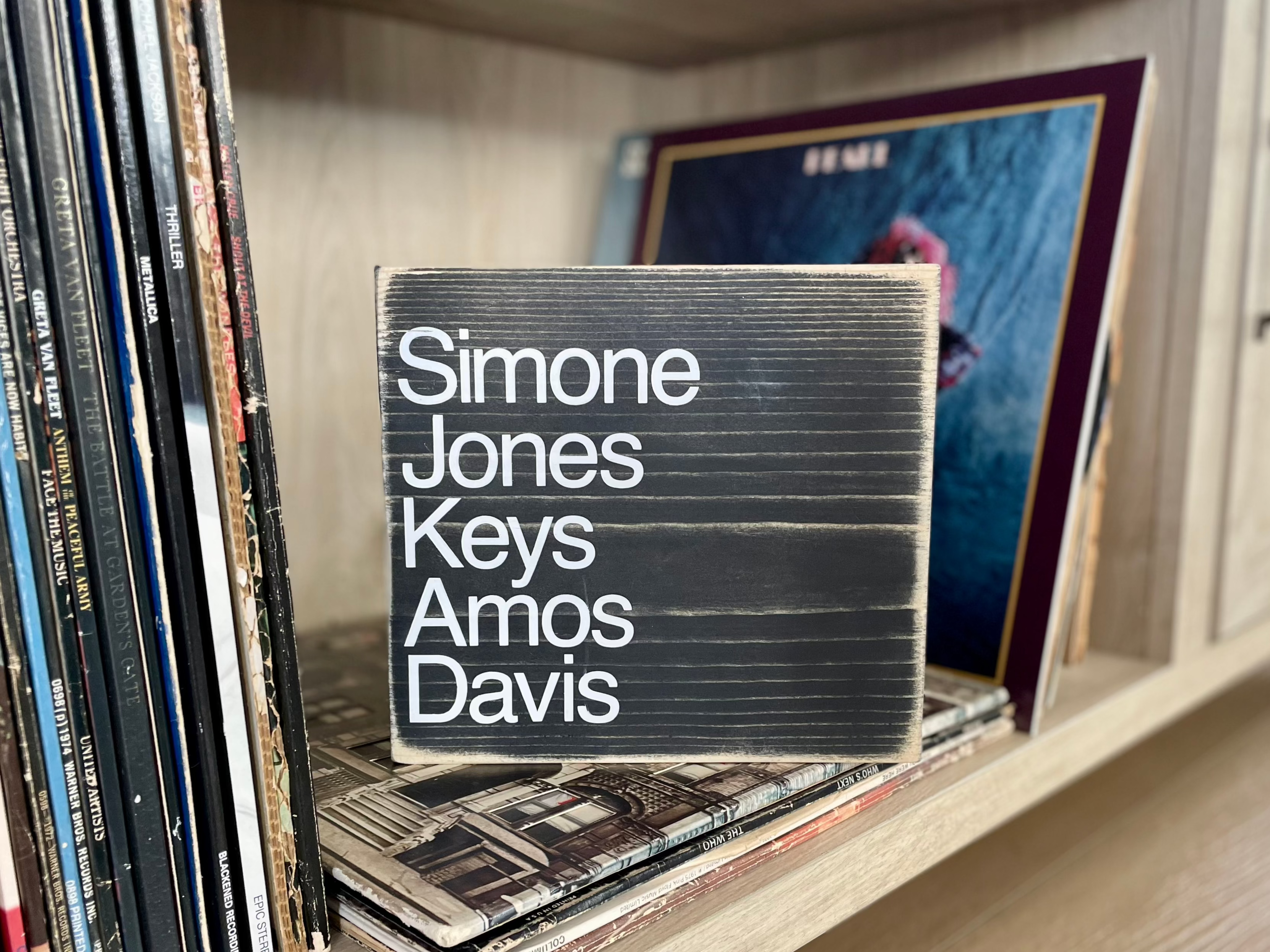 A square, black, wood sign sits on a shelf full of vinyl records