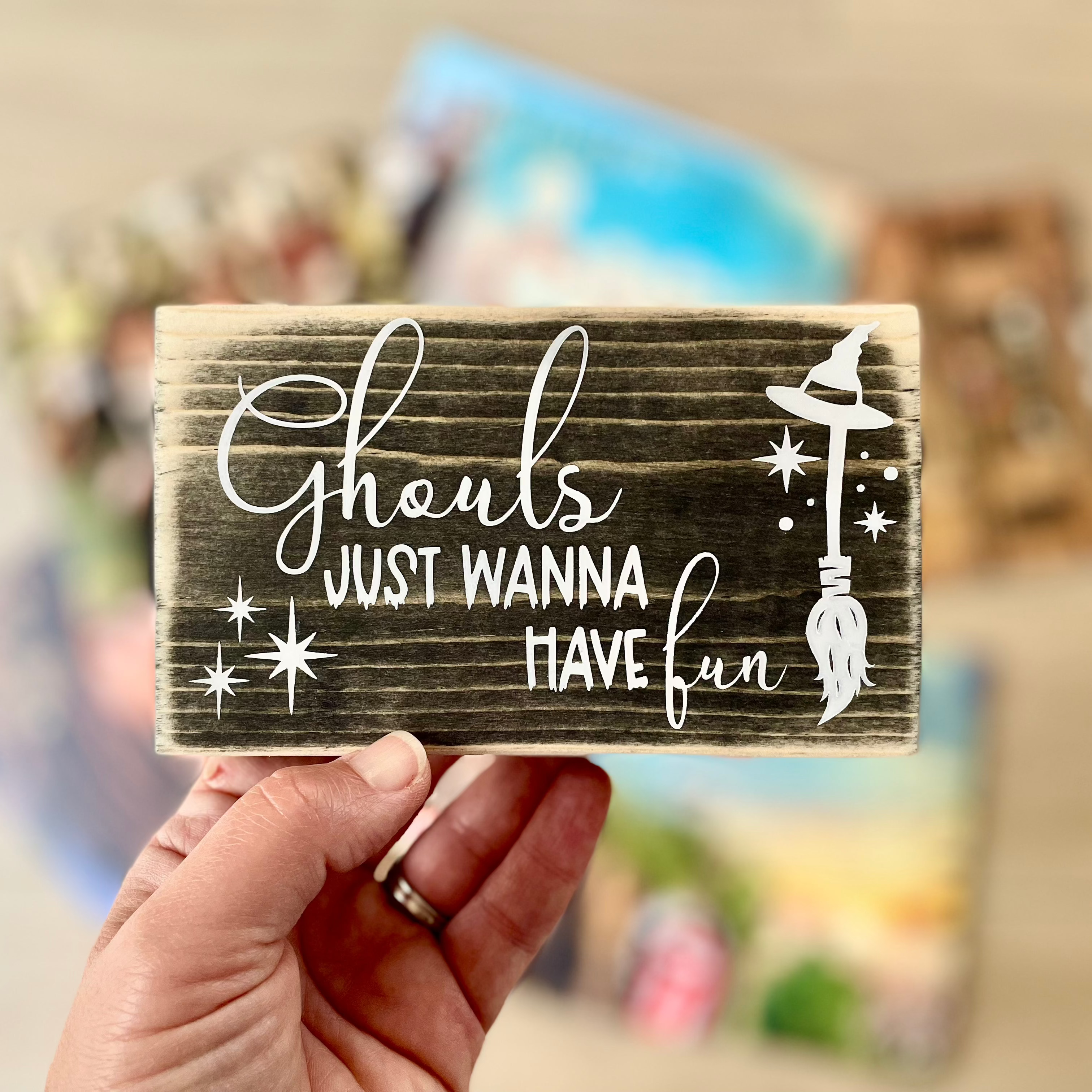 A small, black, wood sign is being held; several vinyl records are blurred in the background