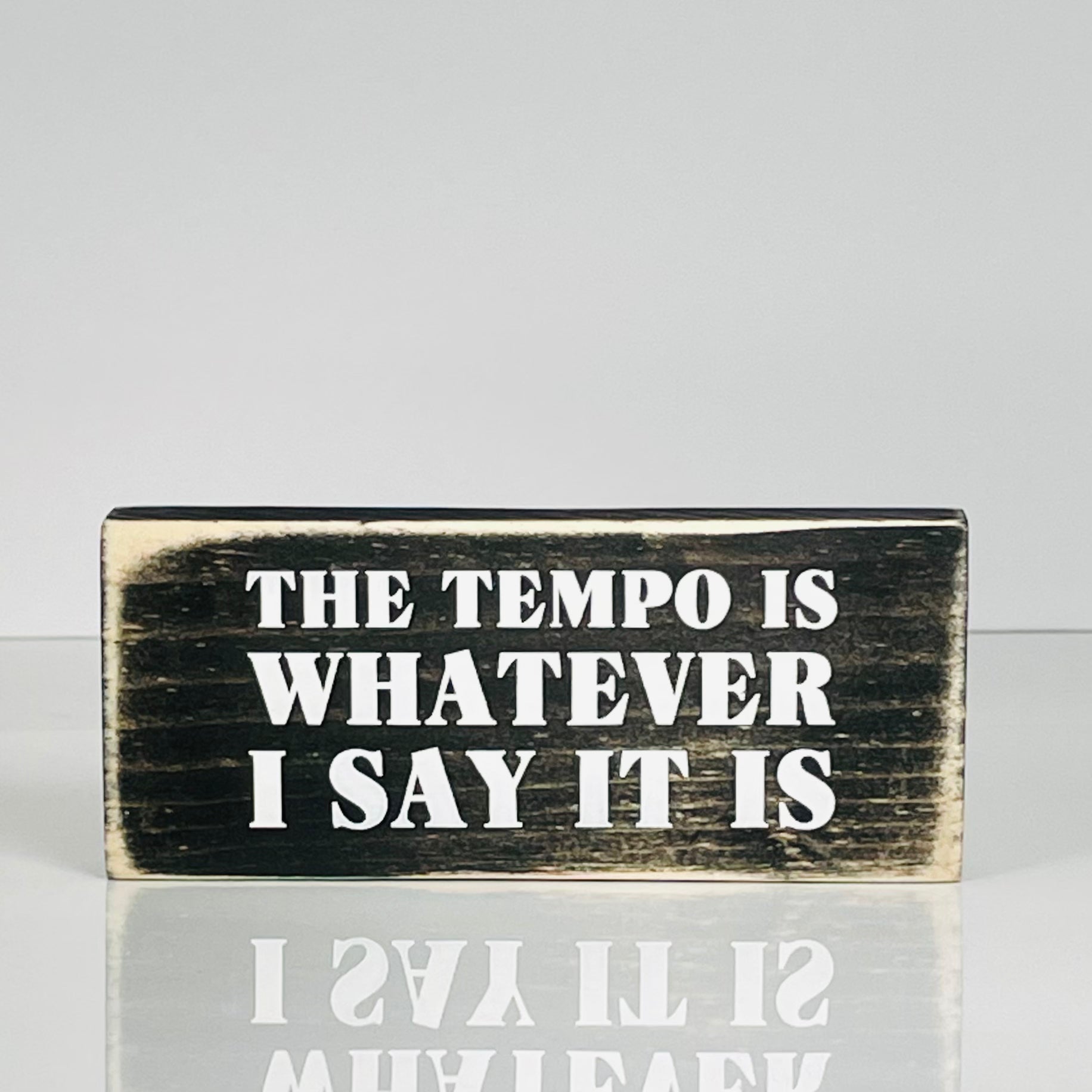 A small, black, wood sign sits on a white surface.