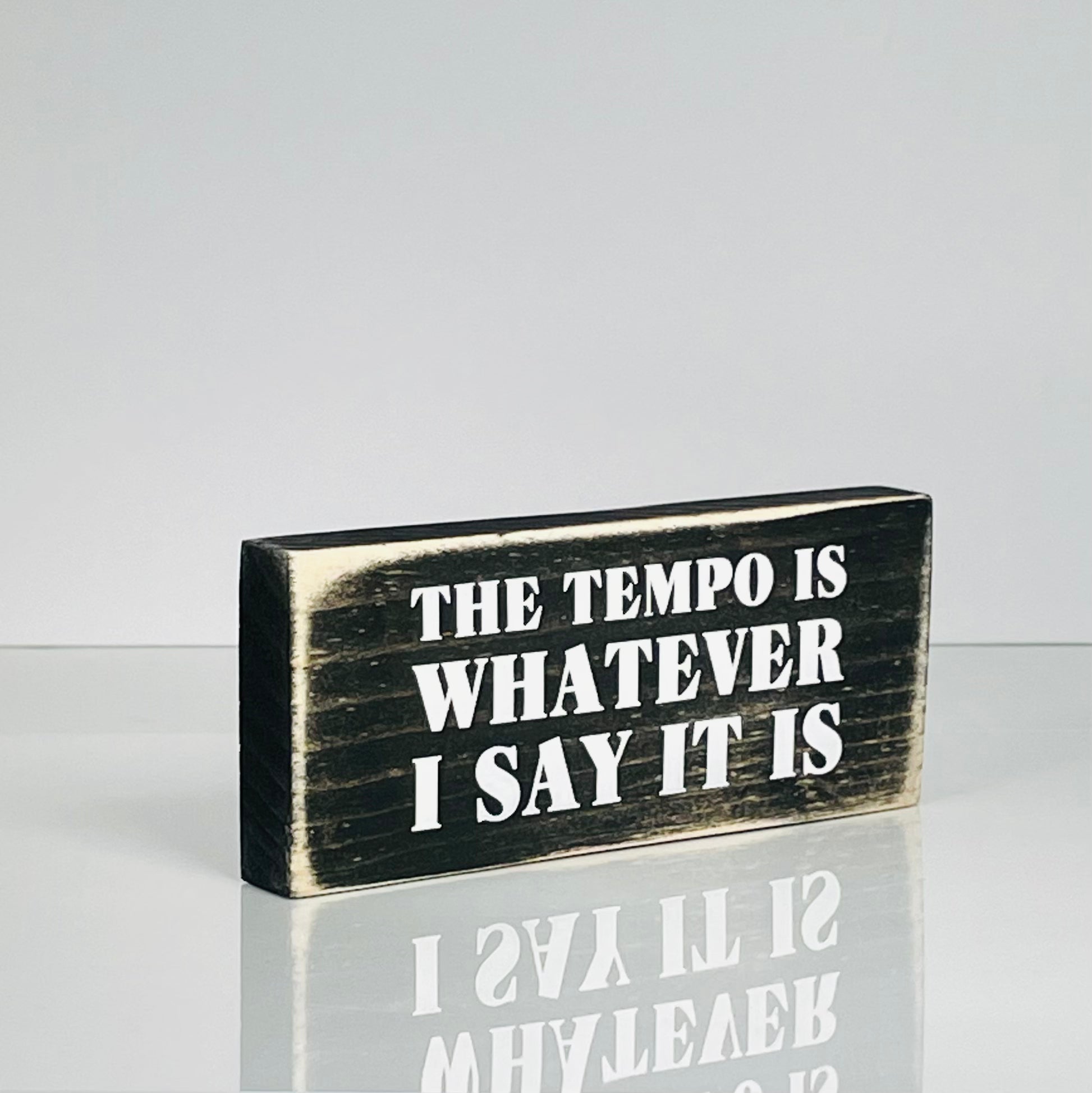 A small, black, wood sign sits on a white surface.