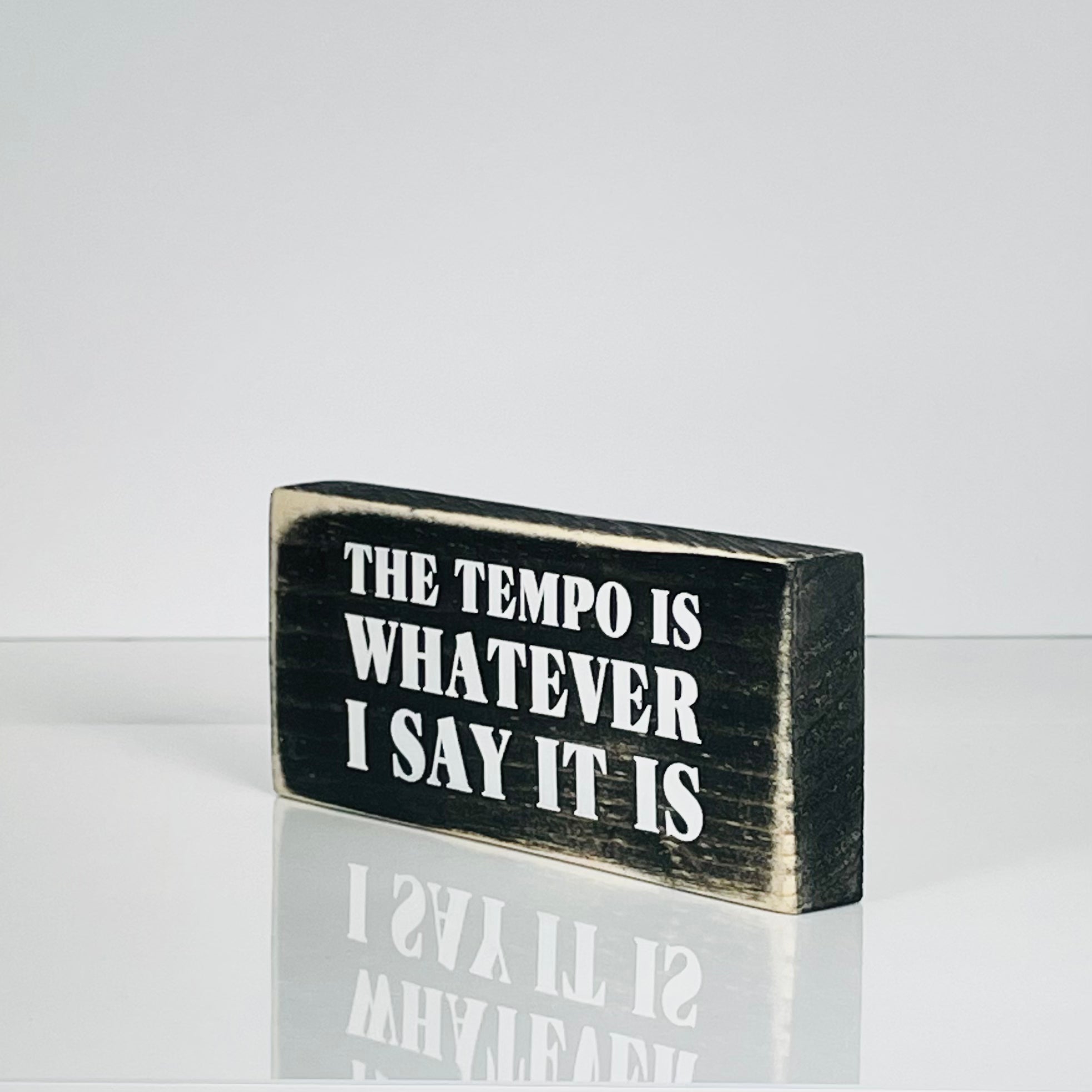 A small, black, wood sign sits on a white surface.