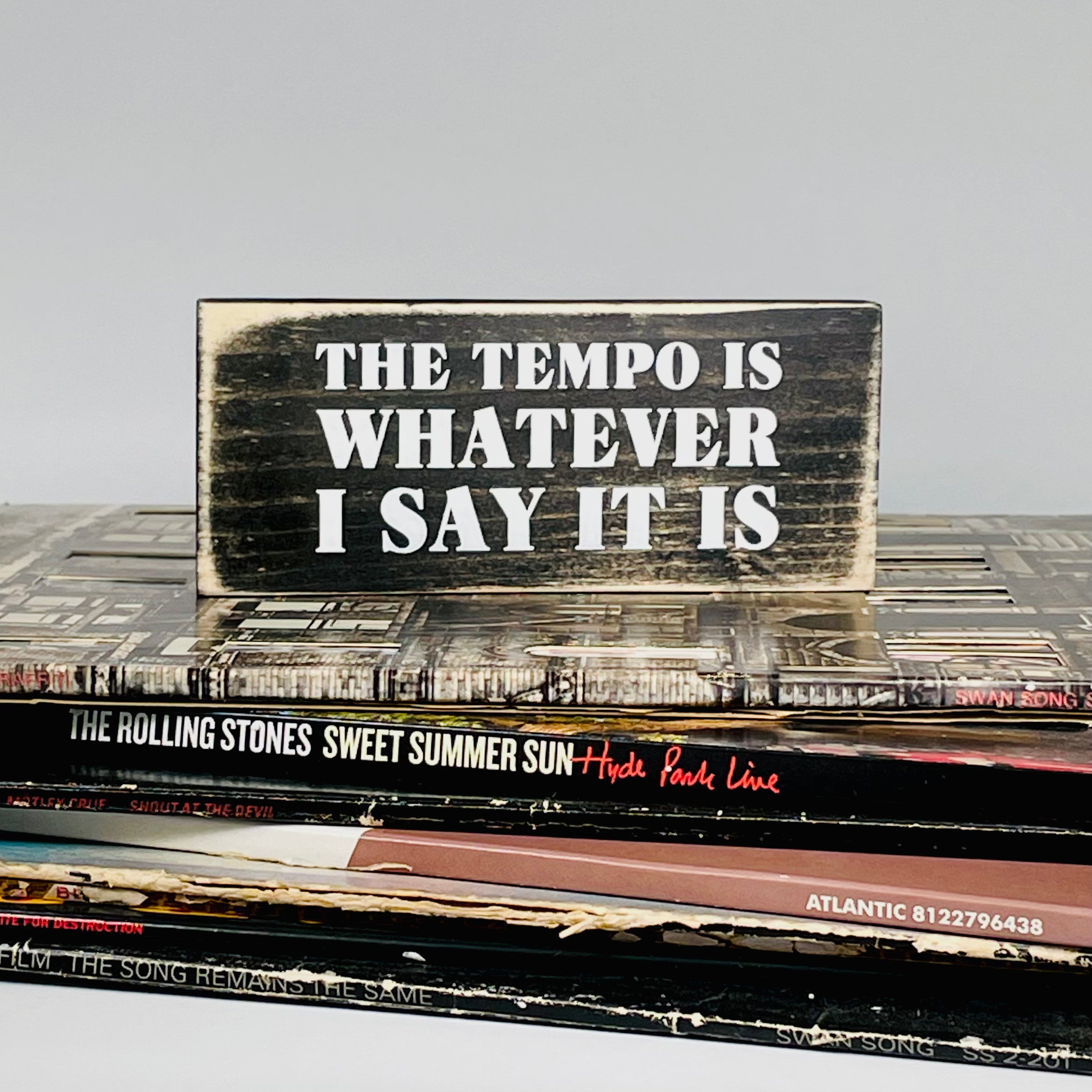 small rectangular wood sign stained black with white lettering that reads "the tempo is whatever i say it is" in all caps on three lines of text.