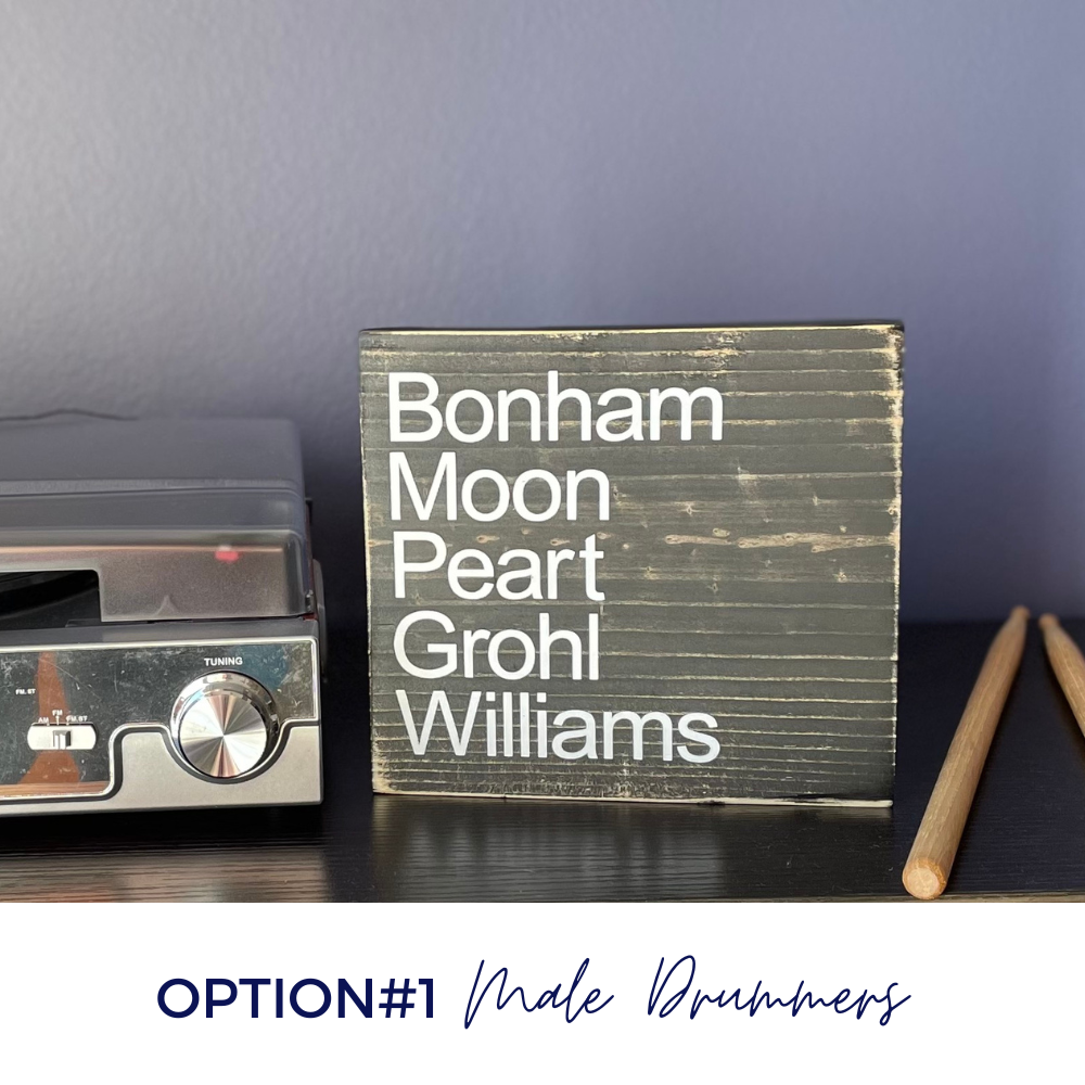 A black wood sign sits on a table with a record player and a pair of drumsticks. The sign reads. "Bonham Moon, Peart, Grohl, Williams". The image shows that this is Option #1.