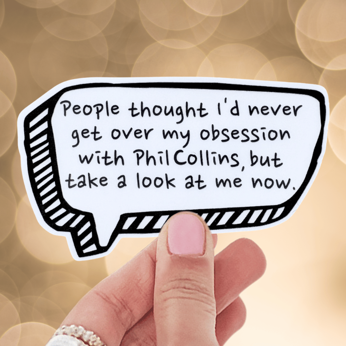 Hand holding a speech bubble with text about obsession with Phil Collins against a blurred background