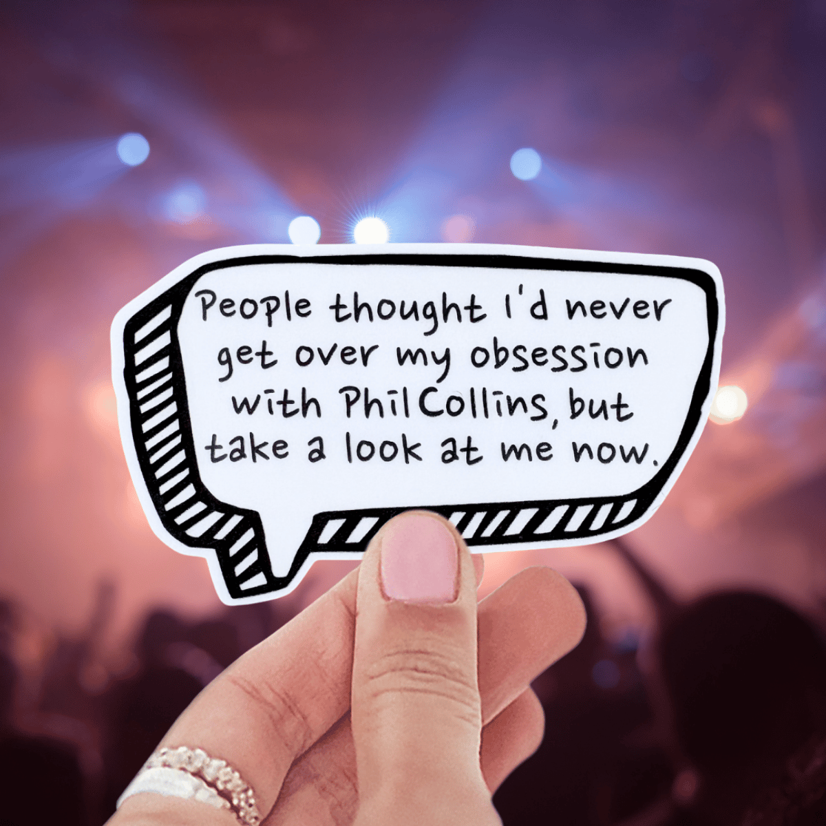 Hand holding a speech bubble with text in front of a blurred concert background