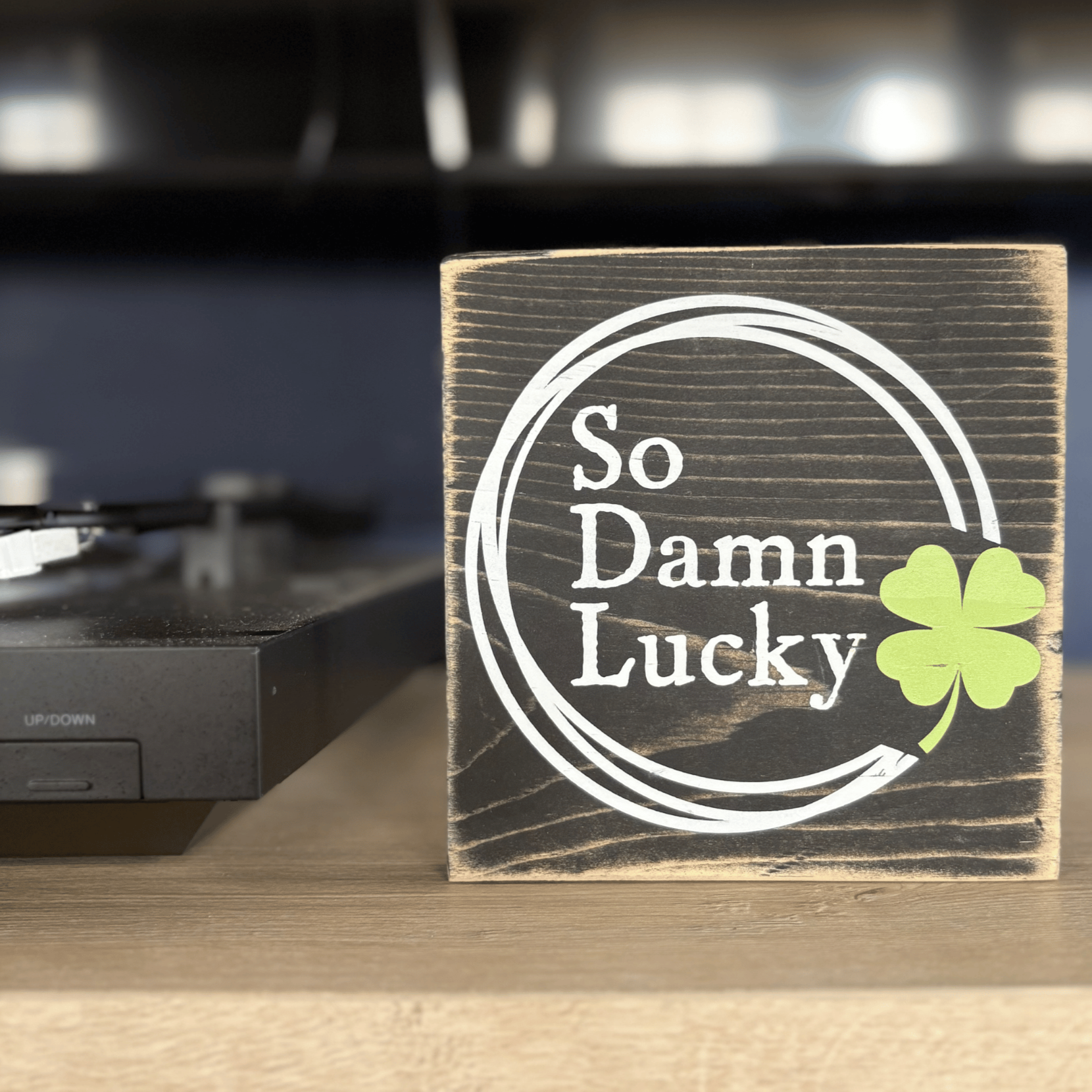 Wooden block with 'So Damn Lucky' and a clover leaf on a record player.