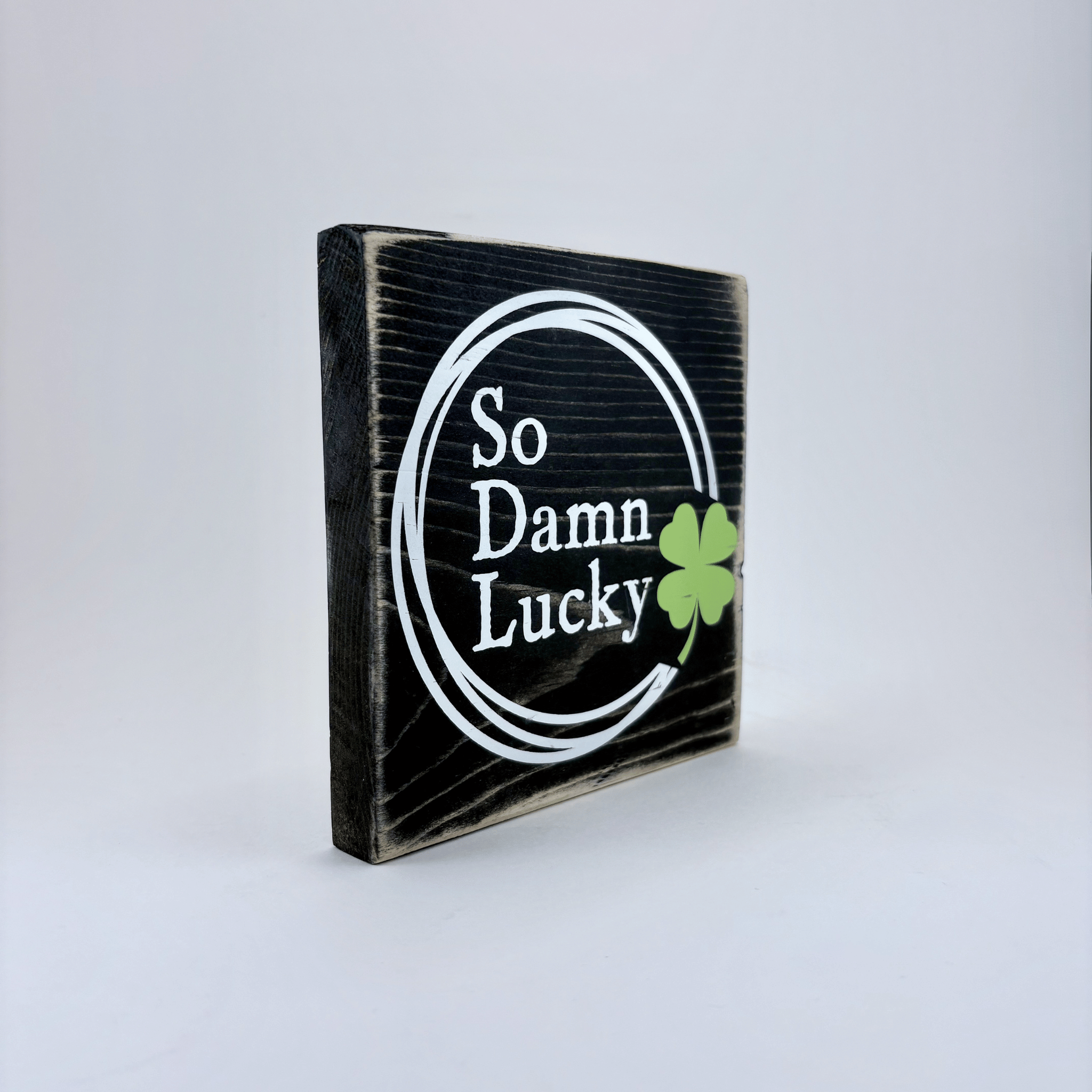 Wooden sign with 'So Damn Lucky' text and a clover leaf on a white background