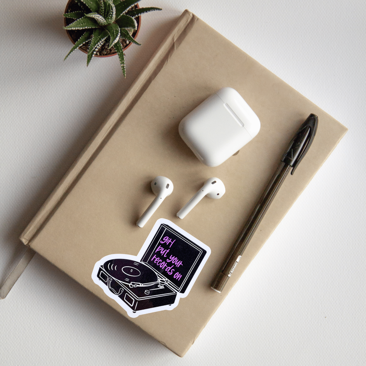 Notebook with AirPods, white case, and a pen on a light surface.