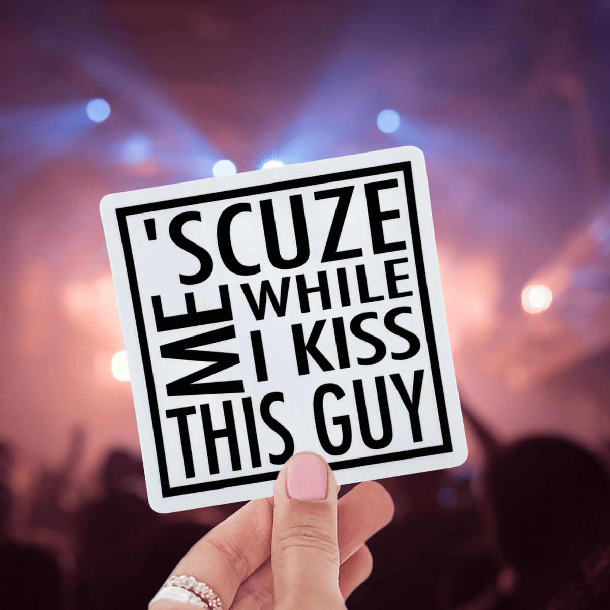 Hand holding a sign with text at a concert with blurred lights in the background