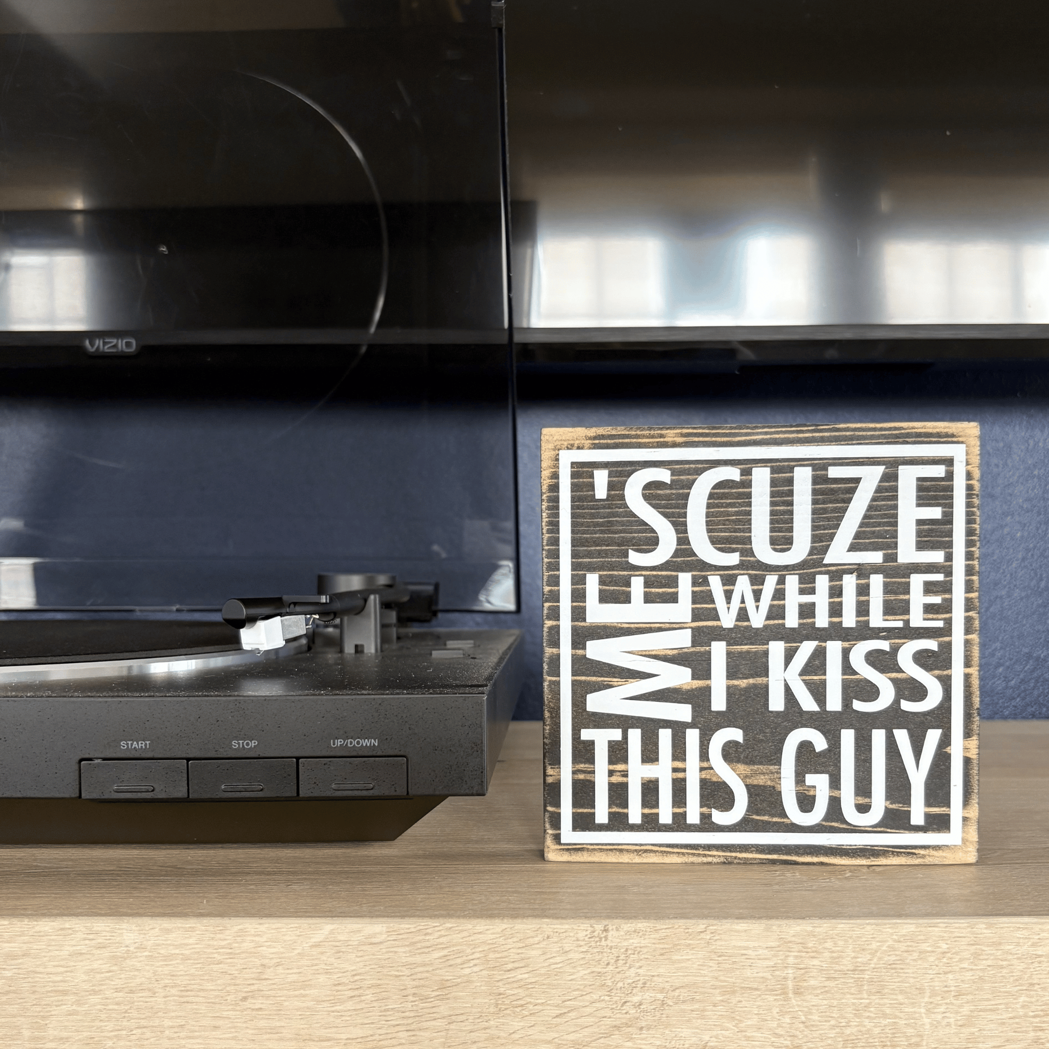 Wooden sign with humorous text next to a record player on a wooden surface.