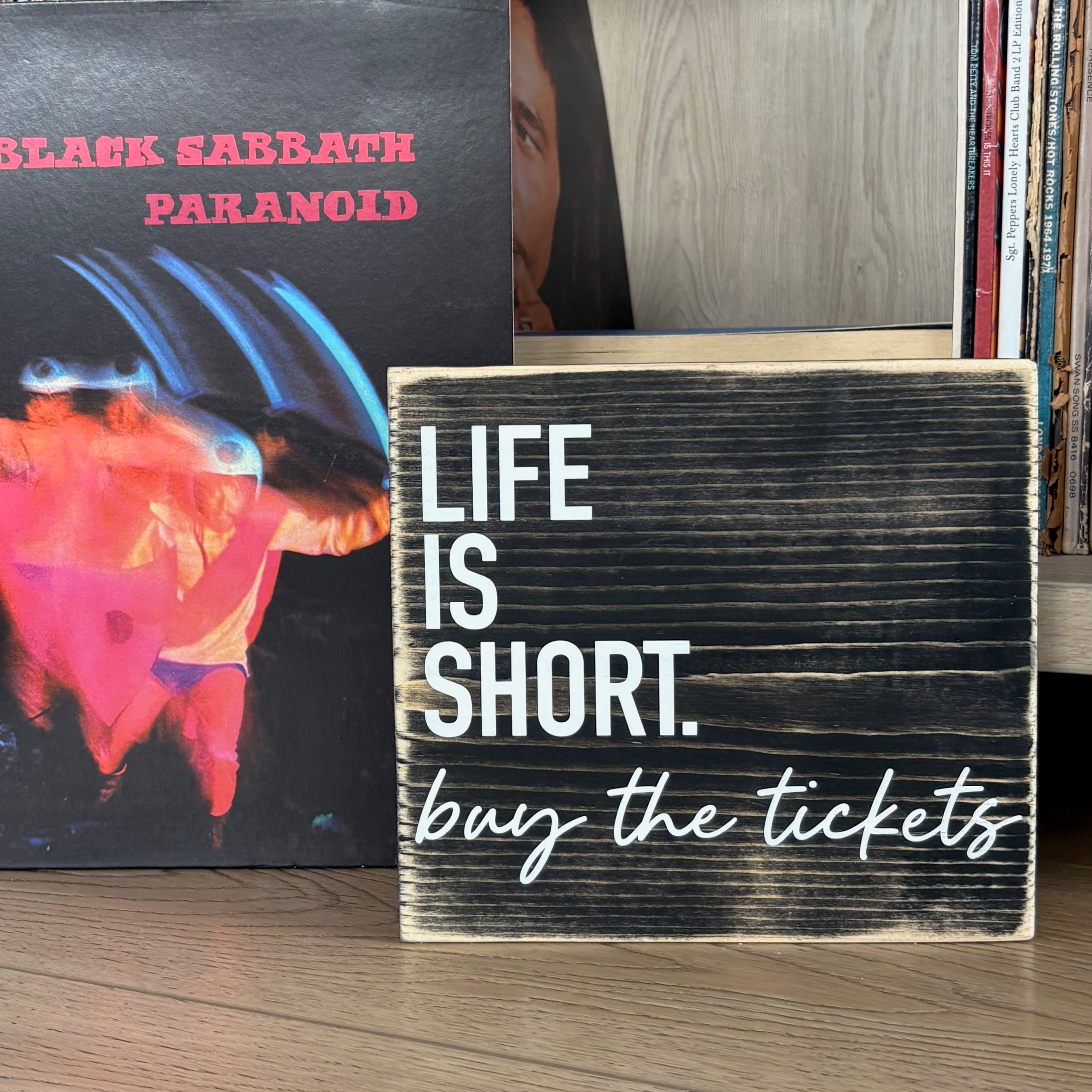 Wooden sign with 'Life is Short, buy the tickets' text in front of vinyl records