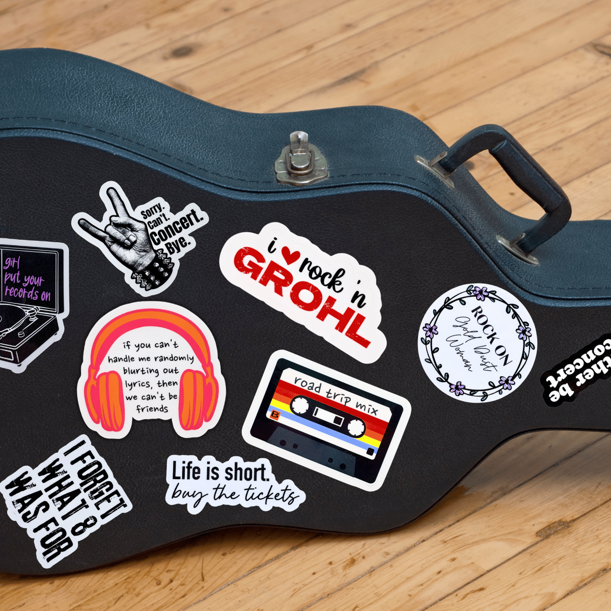 A black guitar case sitting on its side is covered in music themed stickers sold by Three Sisters Studio.