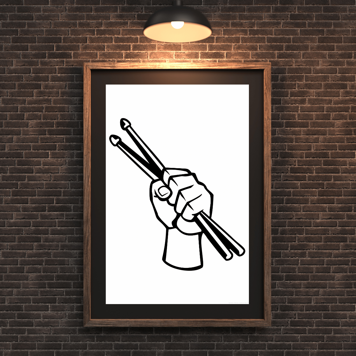 A framed black and white graphic art print of a hand holding drumsticks, mounted on a dark brown brick wall under a lit black ceiling light.
