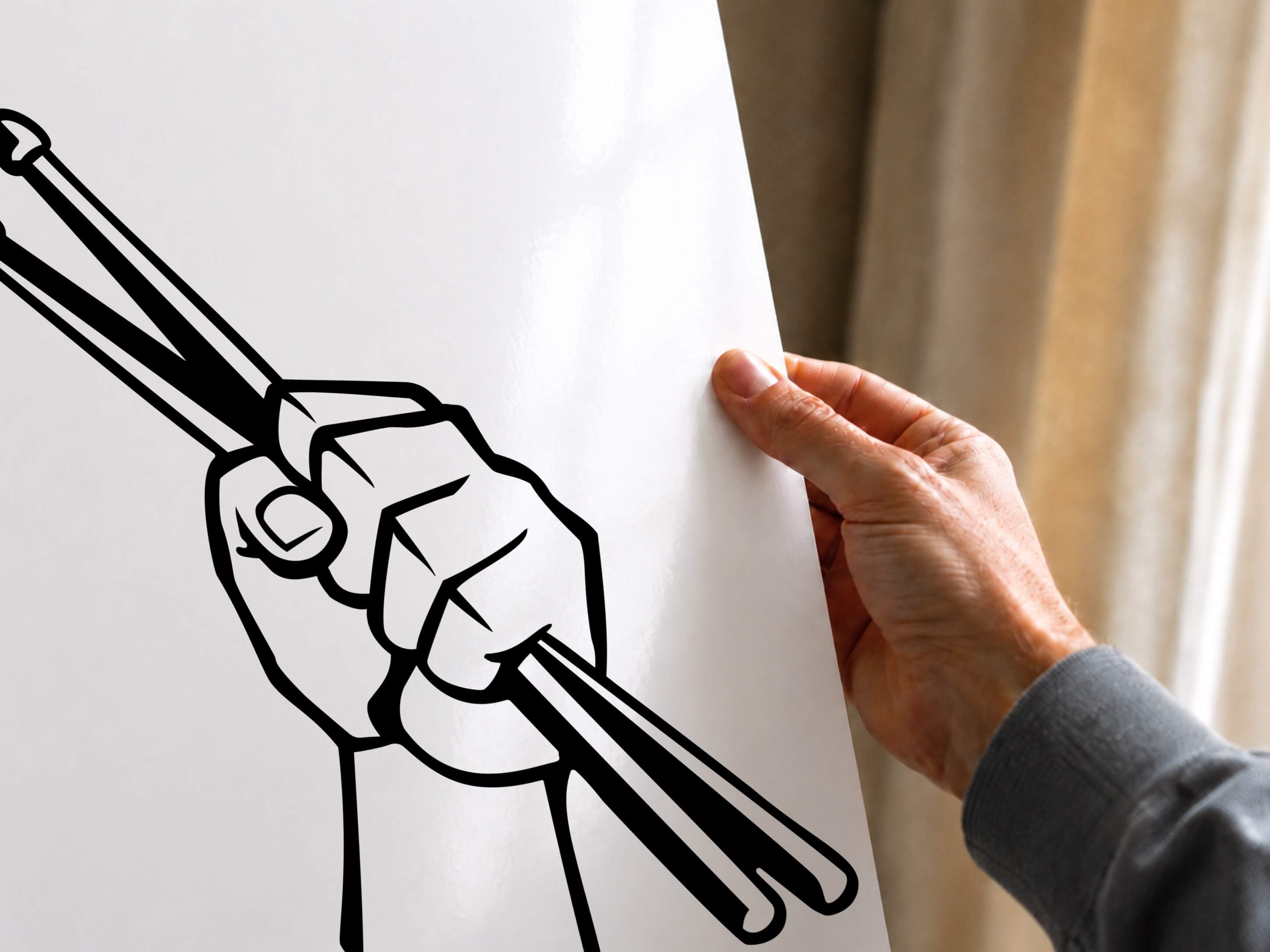 A hand holding a white poster that features a black line art illustration of a hand gripping drumsticks.