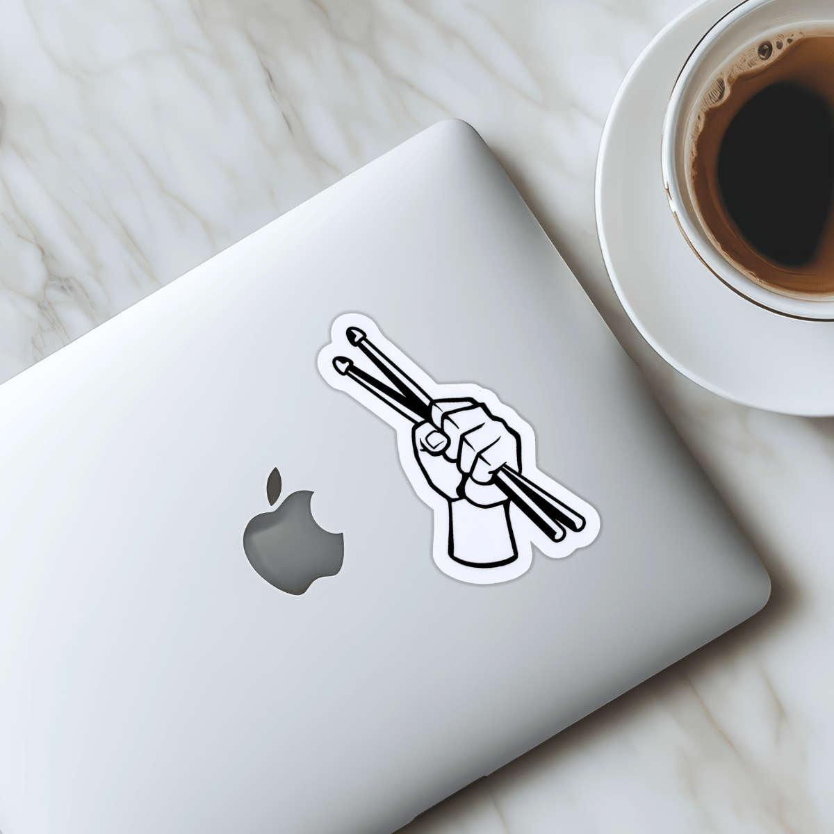 Laptop with a sticker of a hand holding drumsticks next to a cup of coffee on a marble surface