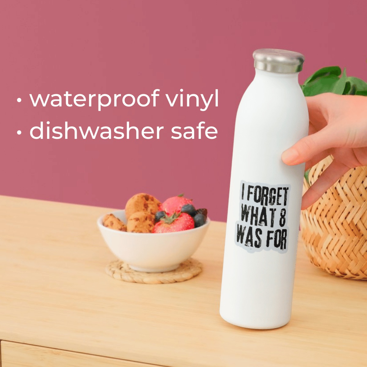 White water bottle with text on a wooden table with a bowl of fruit and a pink background.