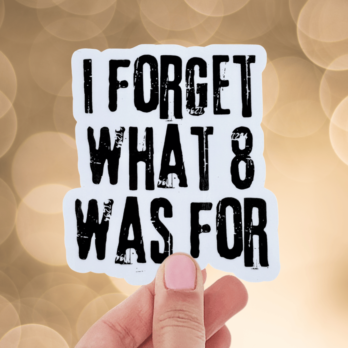 Hand holding a sticker with text 'I FORGET WHAT 8 WAS FOR' against a blurred bokeh background.