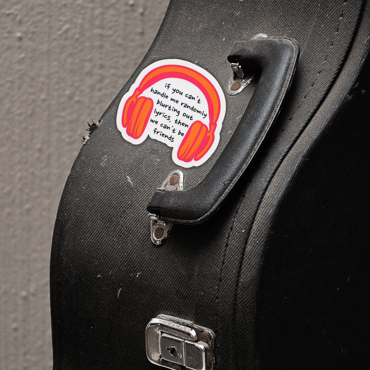 Sticker with headphones and text on a guitar case.
