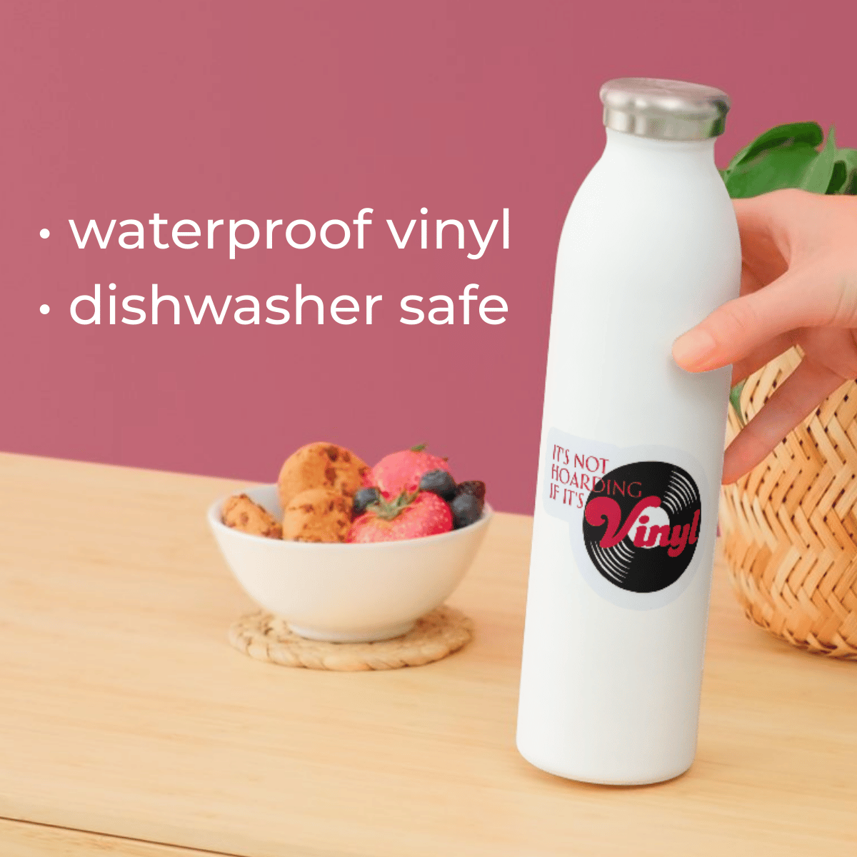 White water bottle with vinyl record design on a wooden table with a bowl of fruit and pink background.