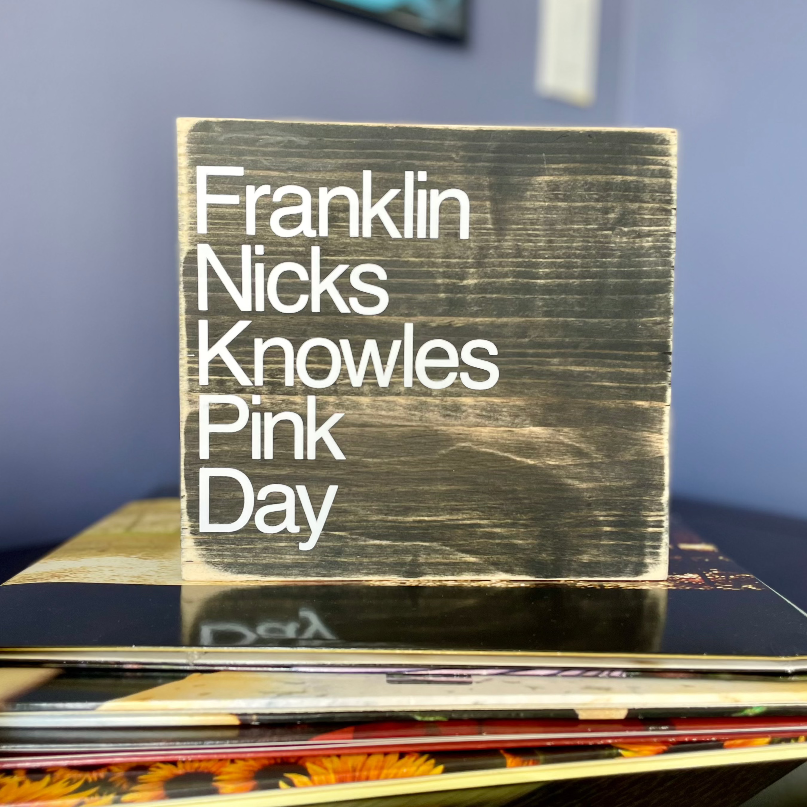 A square, black, wood sign sits on a stack of records.