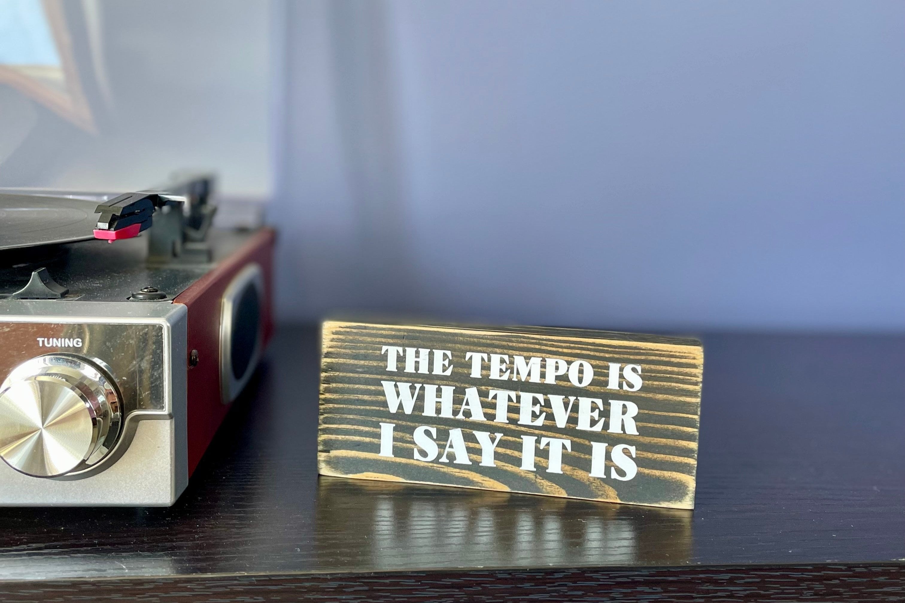 A small, black, wood sign sits on a table next to a record player 