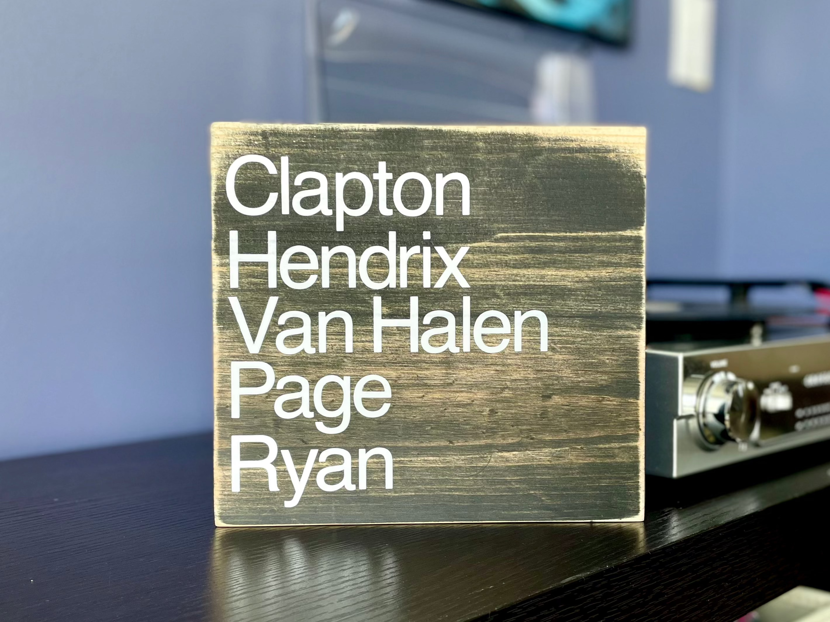 A square, black, wood sign sits on a stack of vinyl records next to a record player.