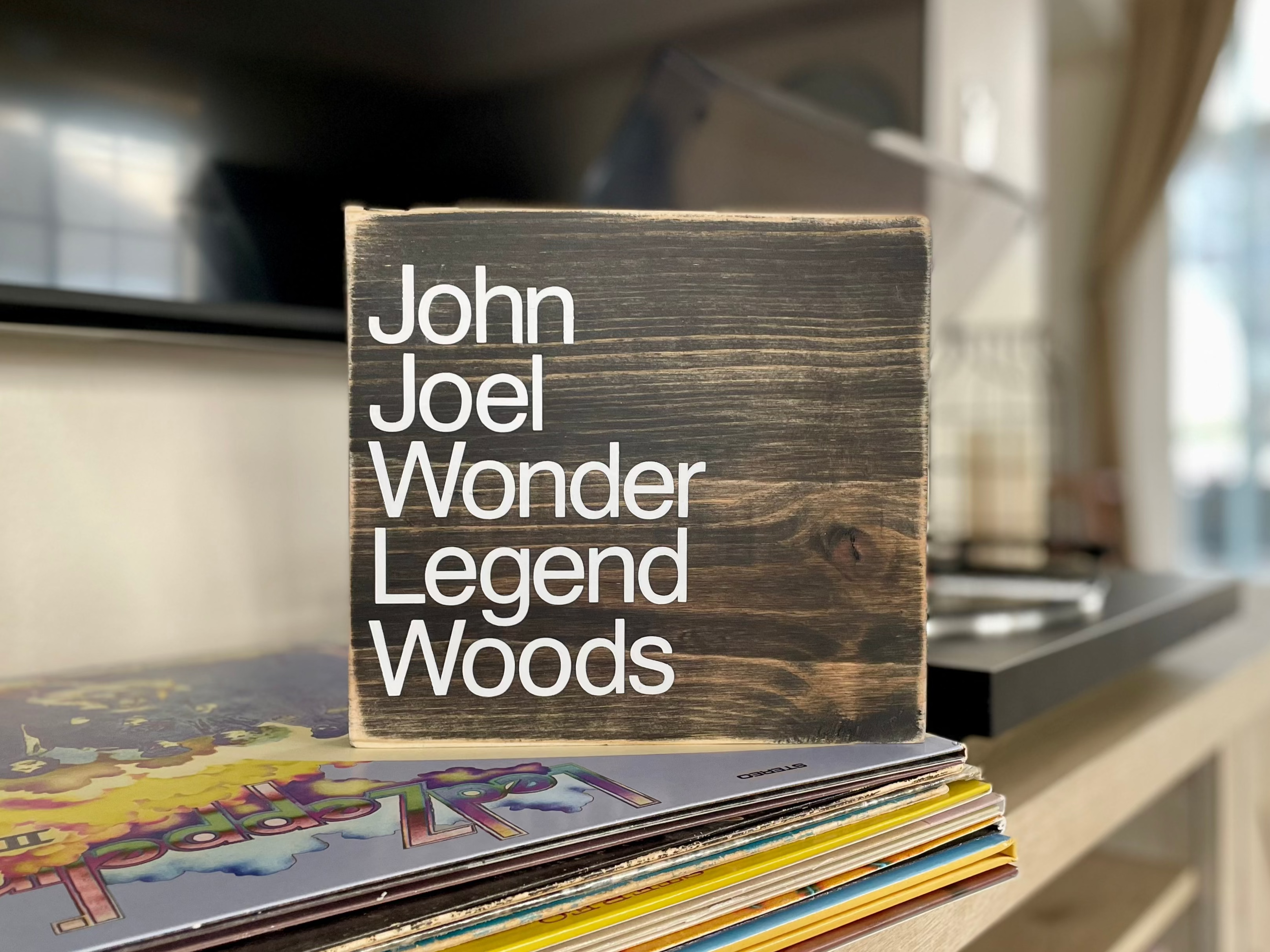 A square, black, wood sign sits on a table next to a record player