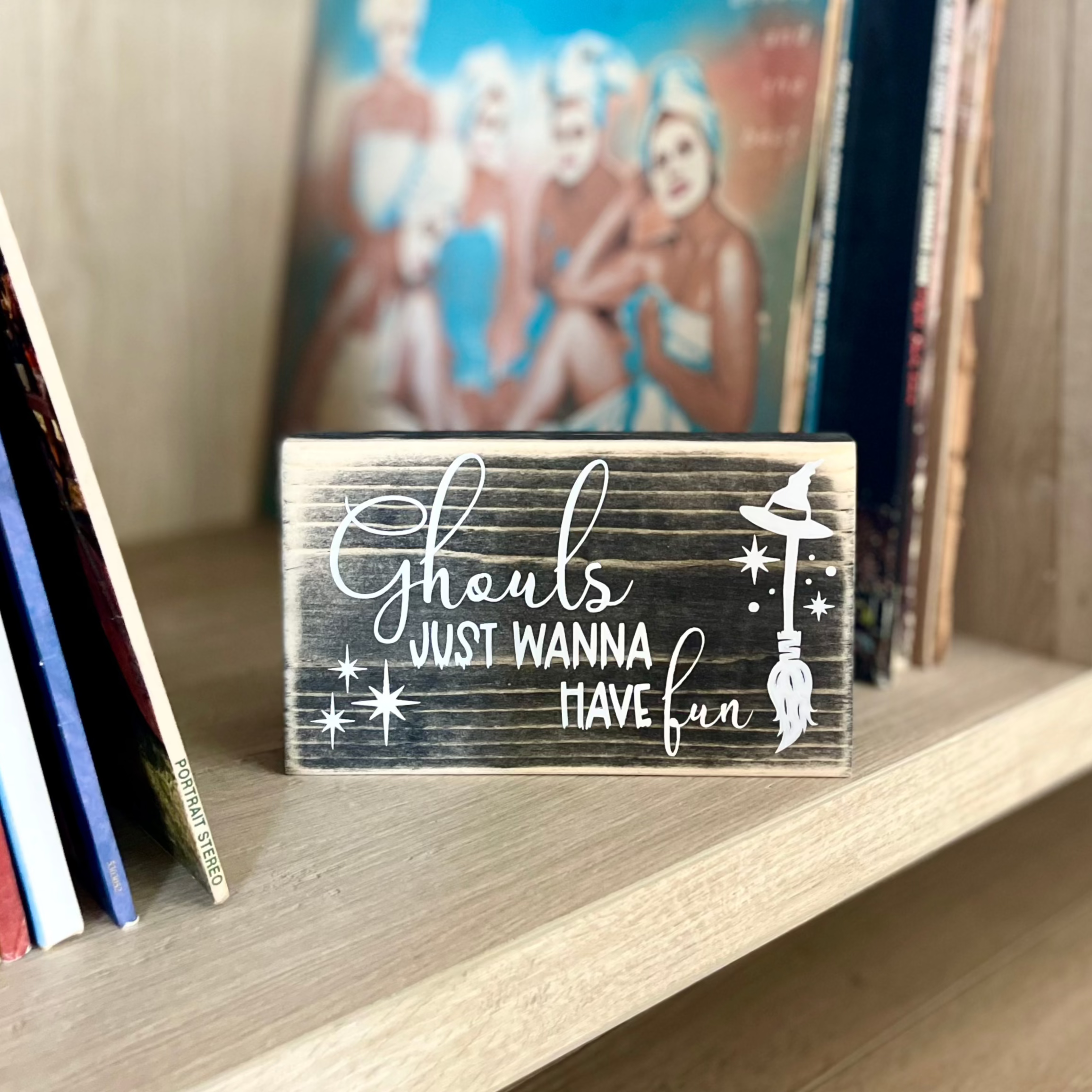 A small, black, wood sign sits on a shelf with stacks of vinyl records. 