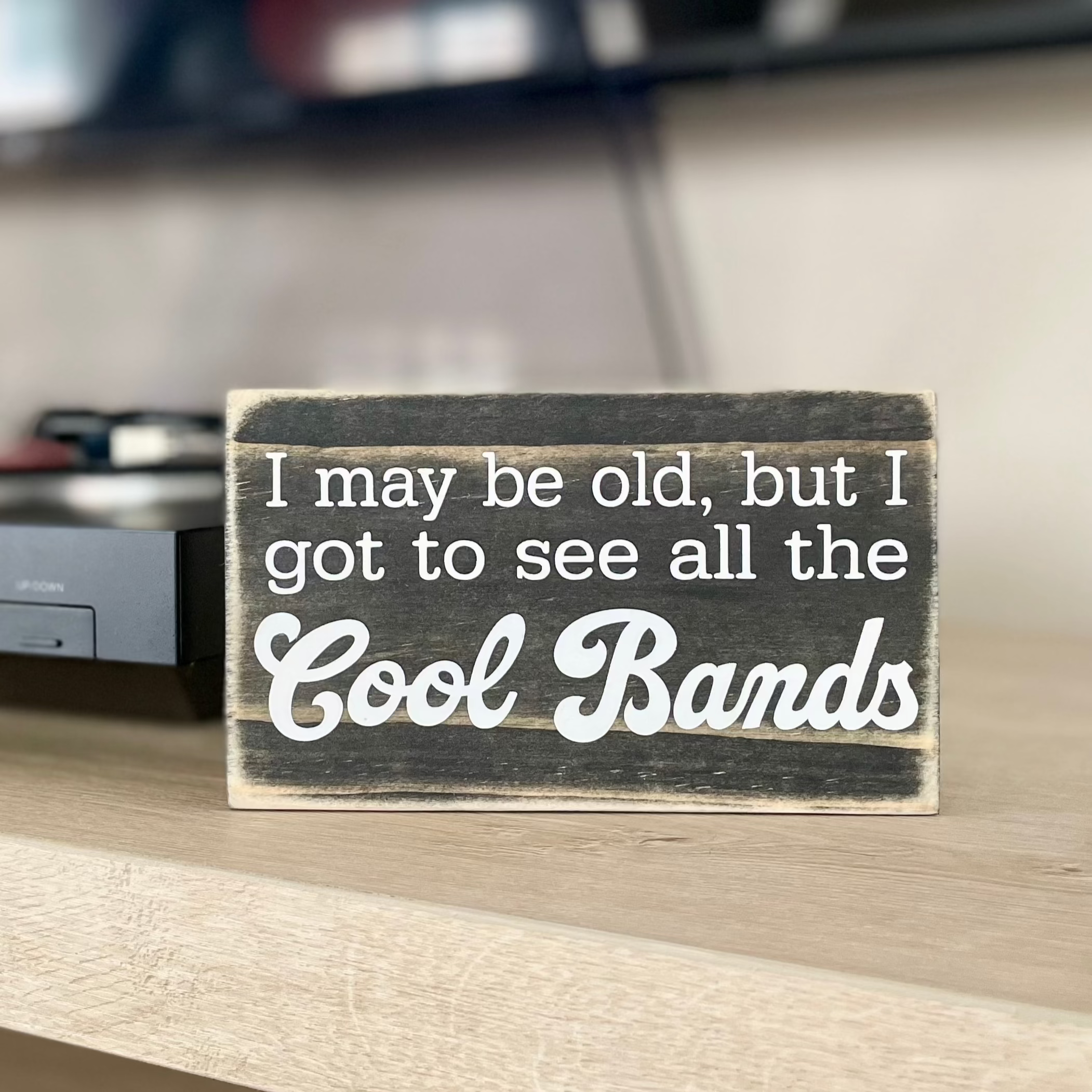 A small, black, wood sign sits on a table next to a record player.