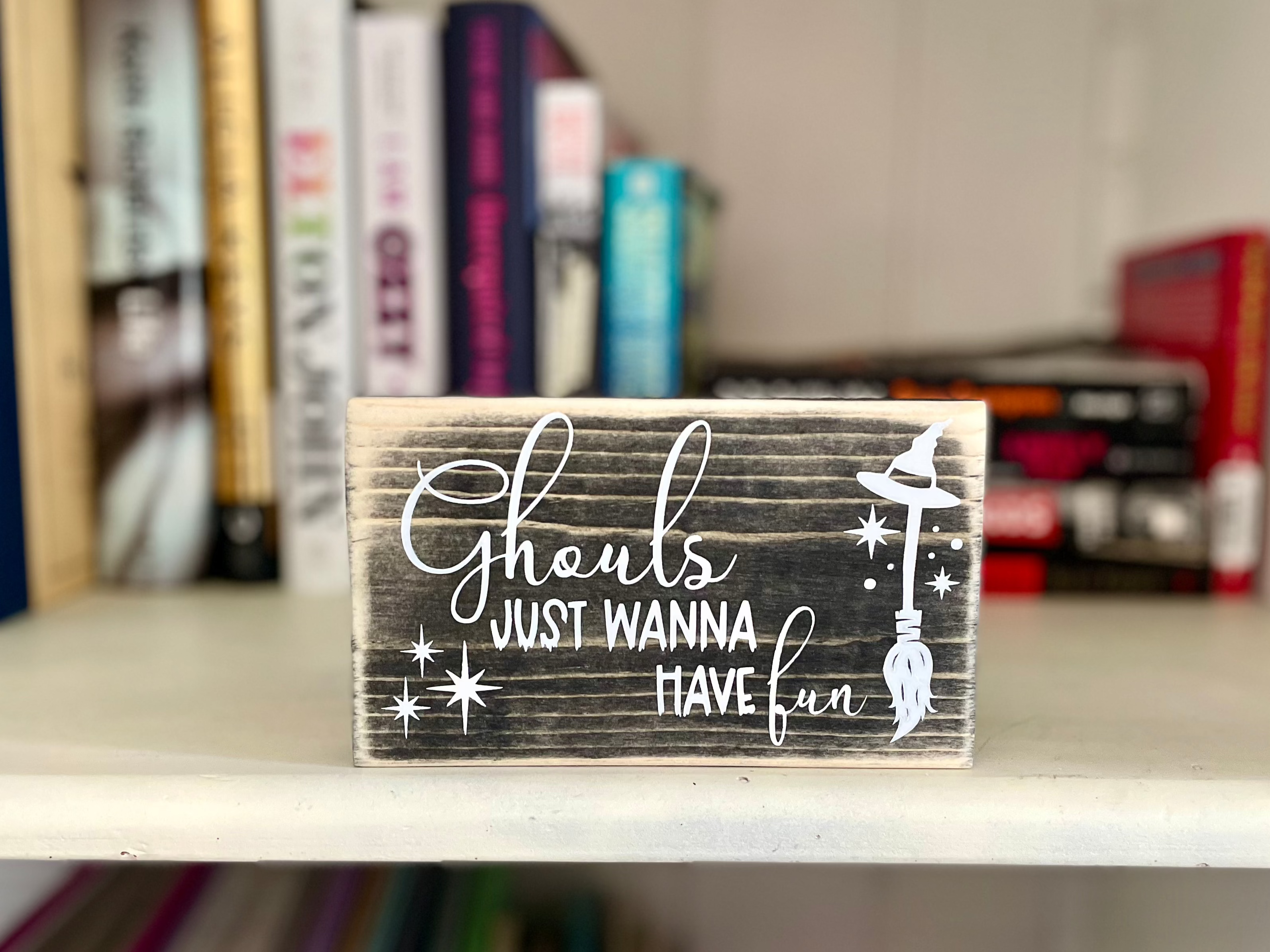 A small, black, wood sign sits on a book shelf with several rock biography books blurred in the background 