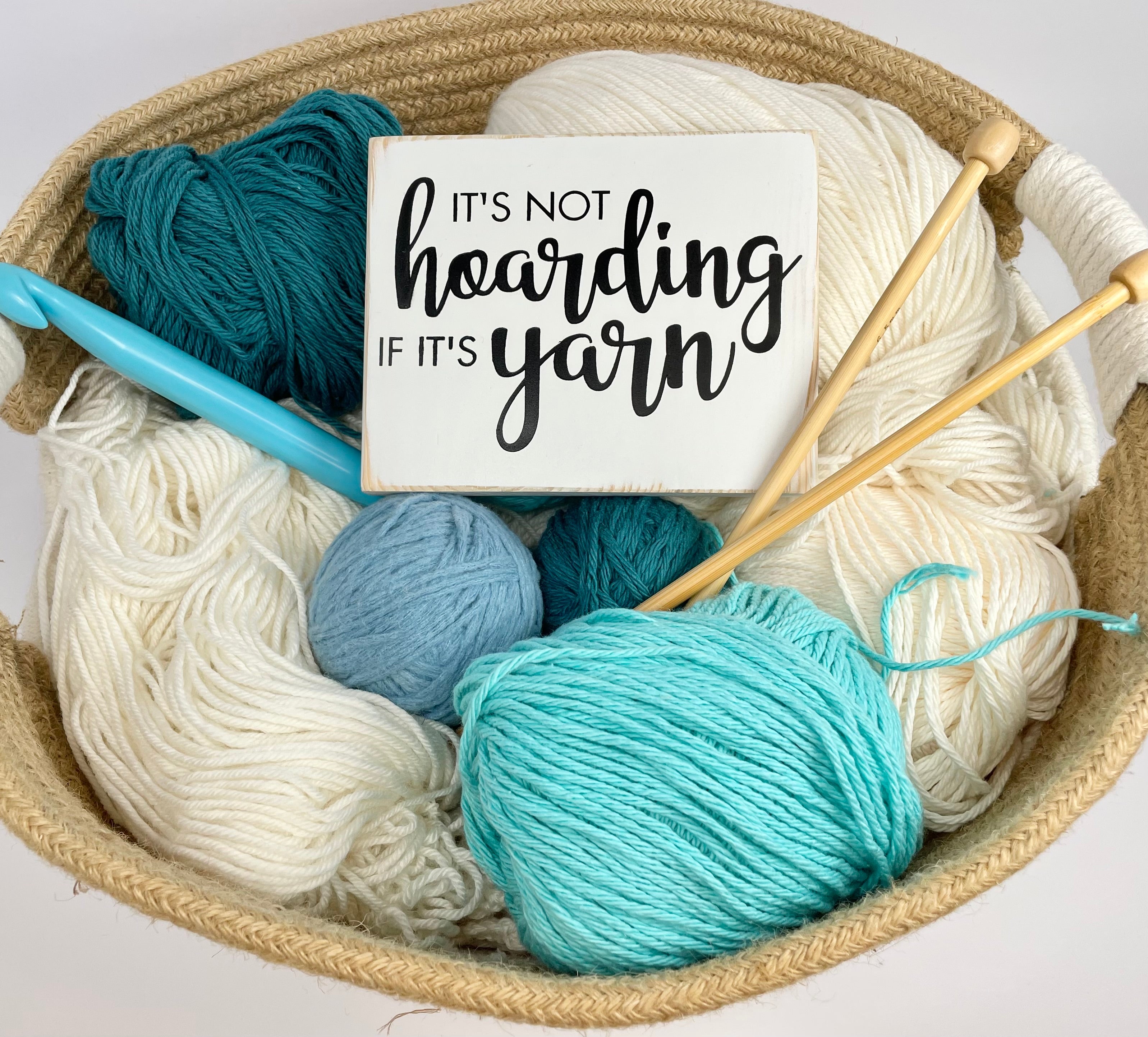 small wood sign painted white with black lettering that reads, "It's not hoarding if it's yarn"