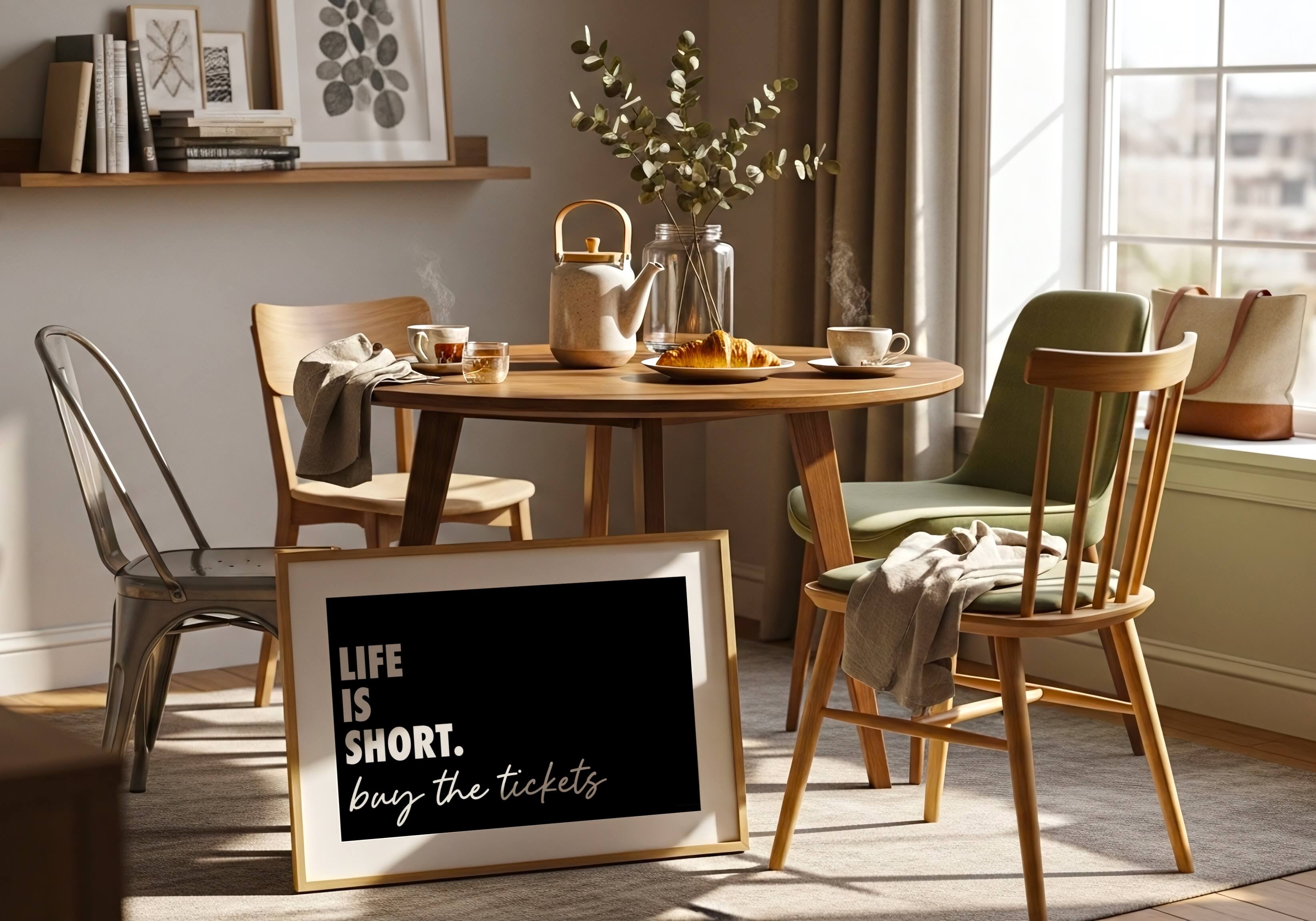 A framed wall art print with the quote 'LIFE IS SHORT. buy the tickets' in white script on a black background, styled in a warm, sunlit dining room next to a wooden table and chairs.