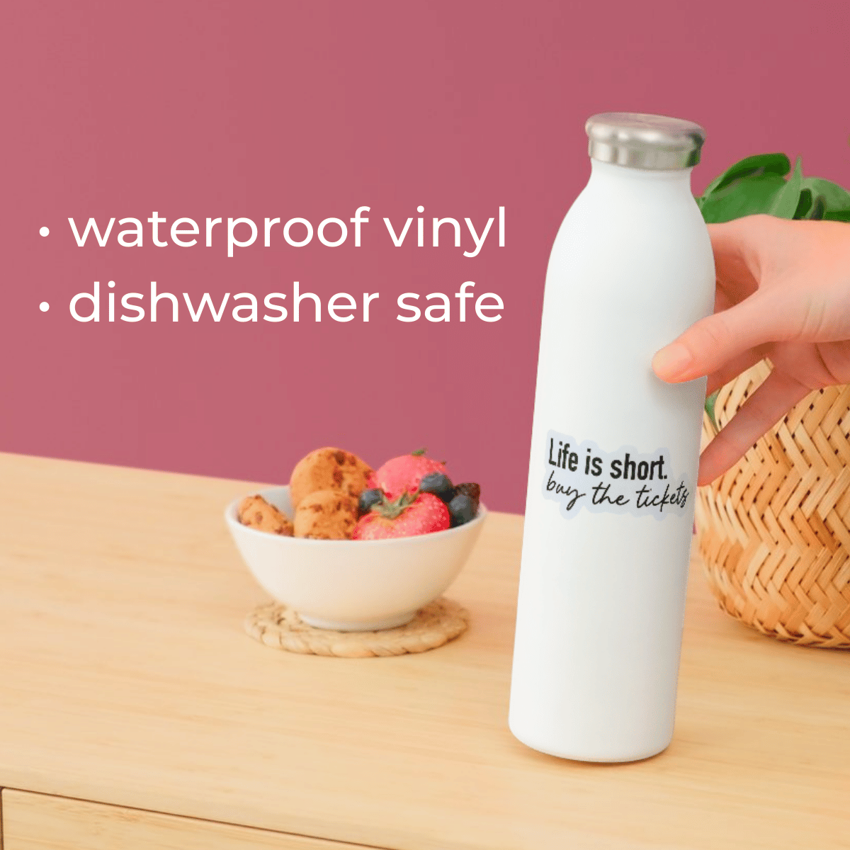 White water bottle with text on a wooden table with a bowl of fruit and a pink background.