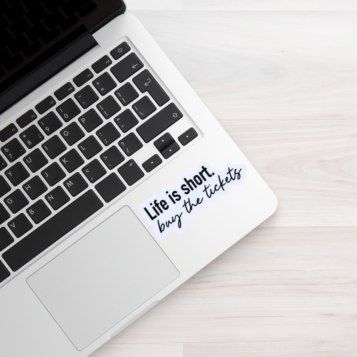 Laptop with a sticker on the palm rest area reading 'Life is short, buy the tickets'.
