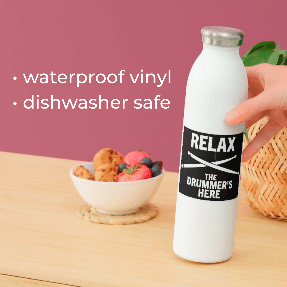 White water bottle with black label featuring text, held by a hand on a wooden surface with a bowl of fruit in the background.