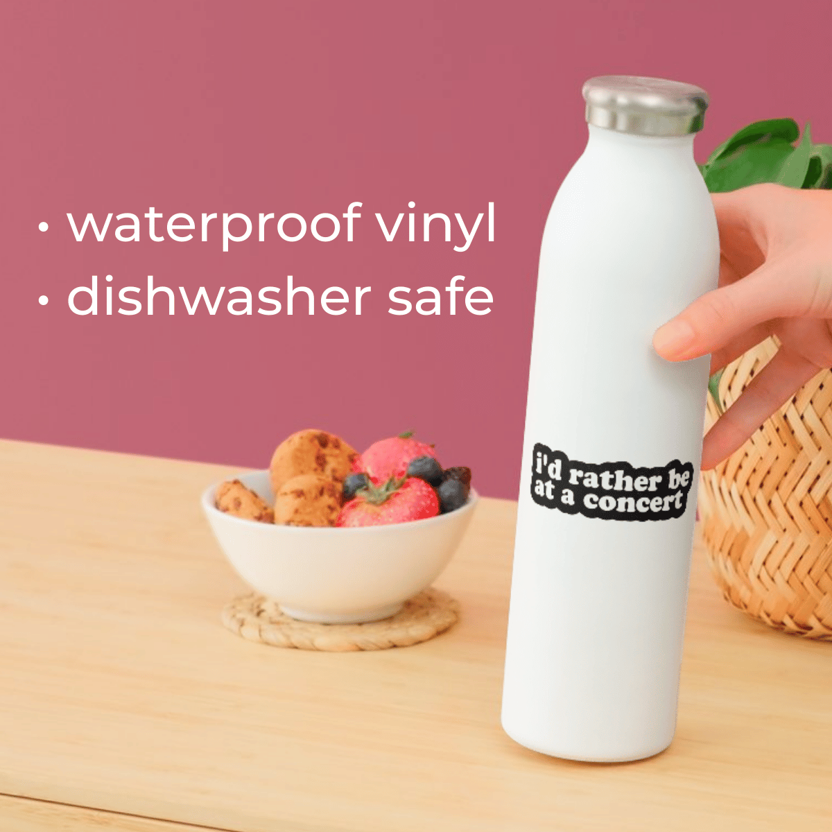 White water bottle with text on a wooden table with a bowl of fruit and a pink background.